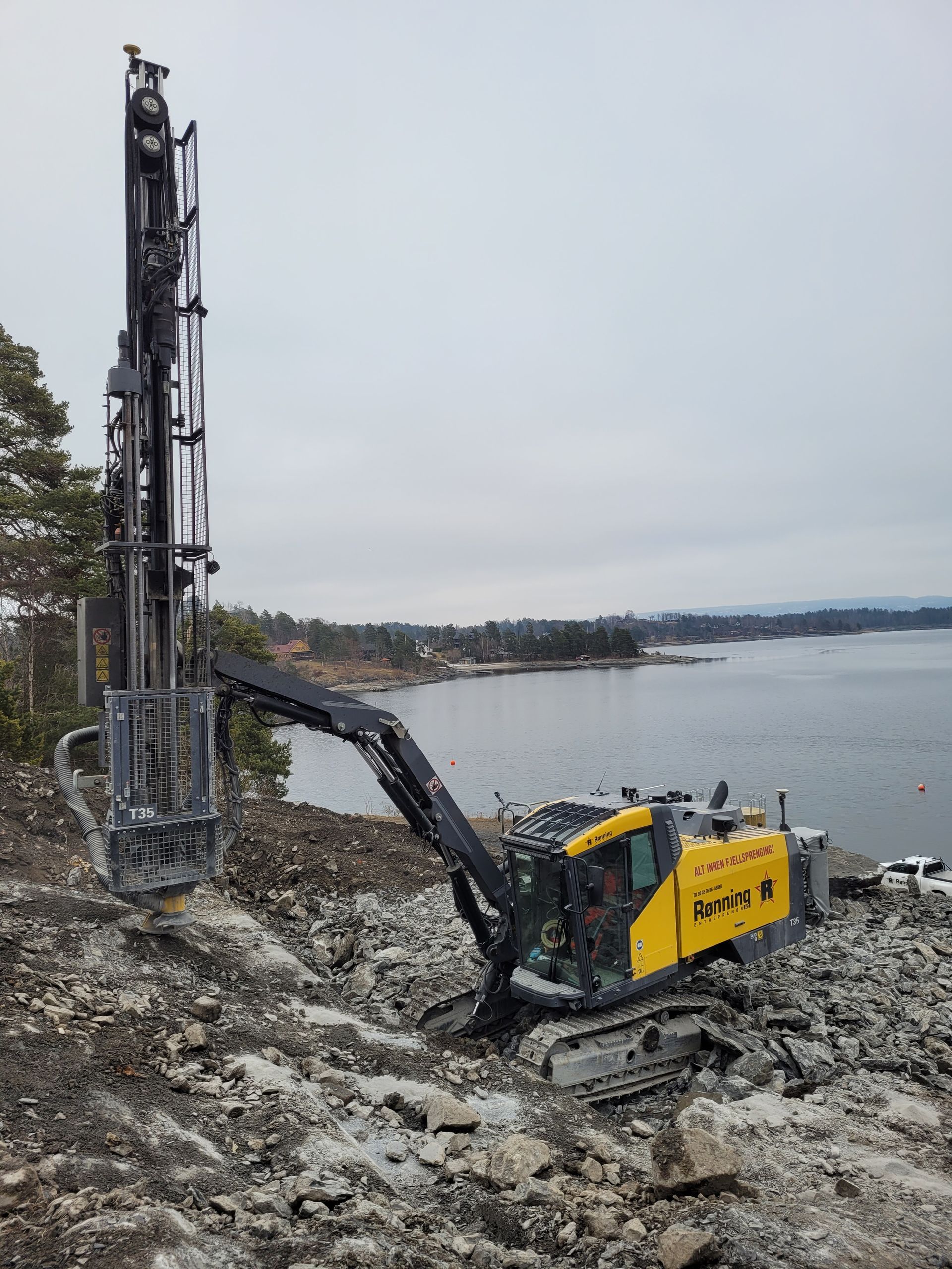 Gul borerigg på steinete grunn med utsikt over vann.