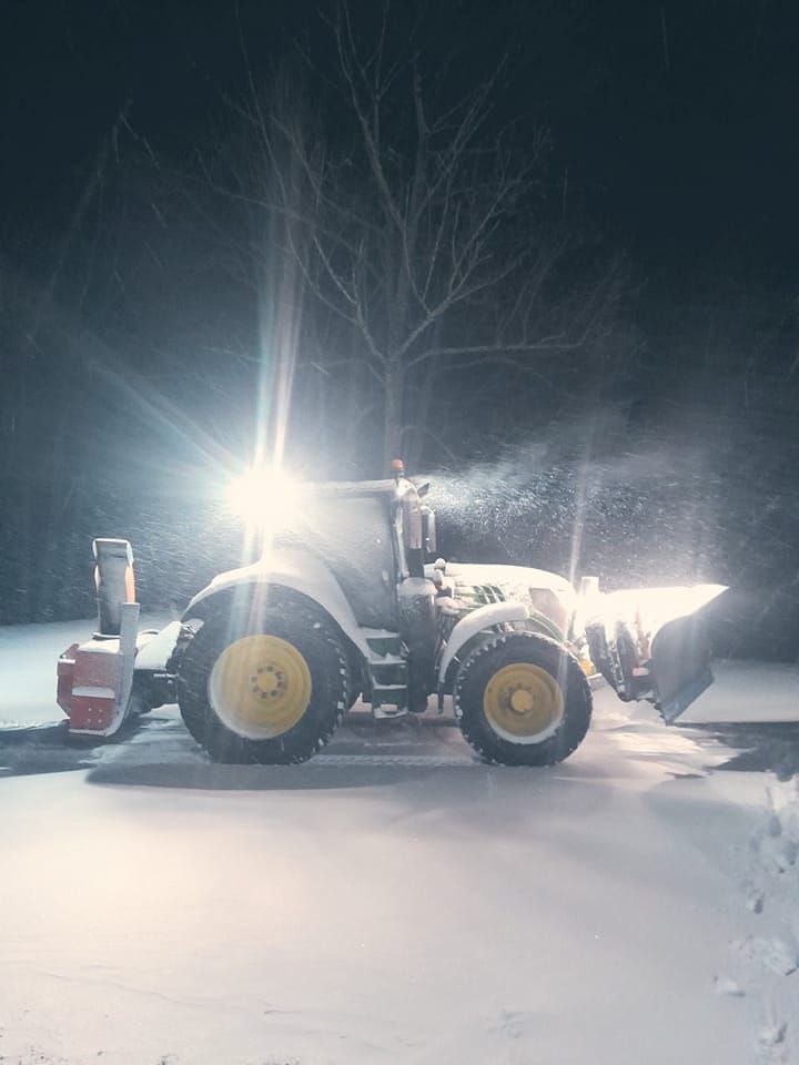 Snødekt traktor med sterke frontlykter rydder snø om natten.