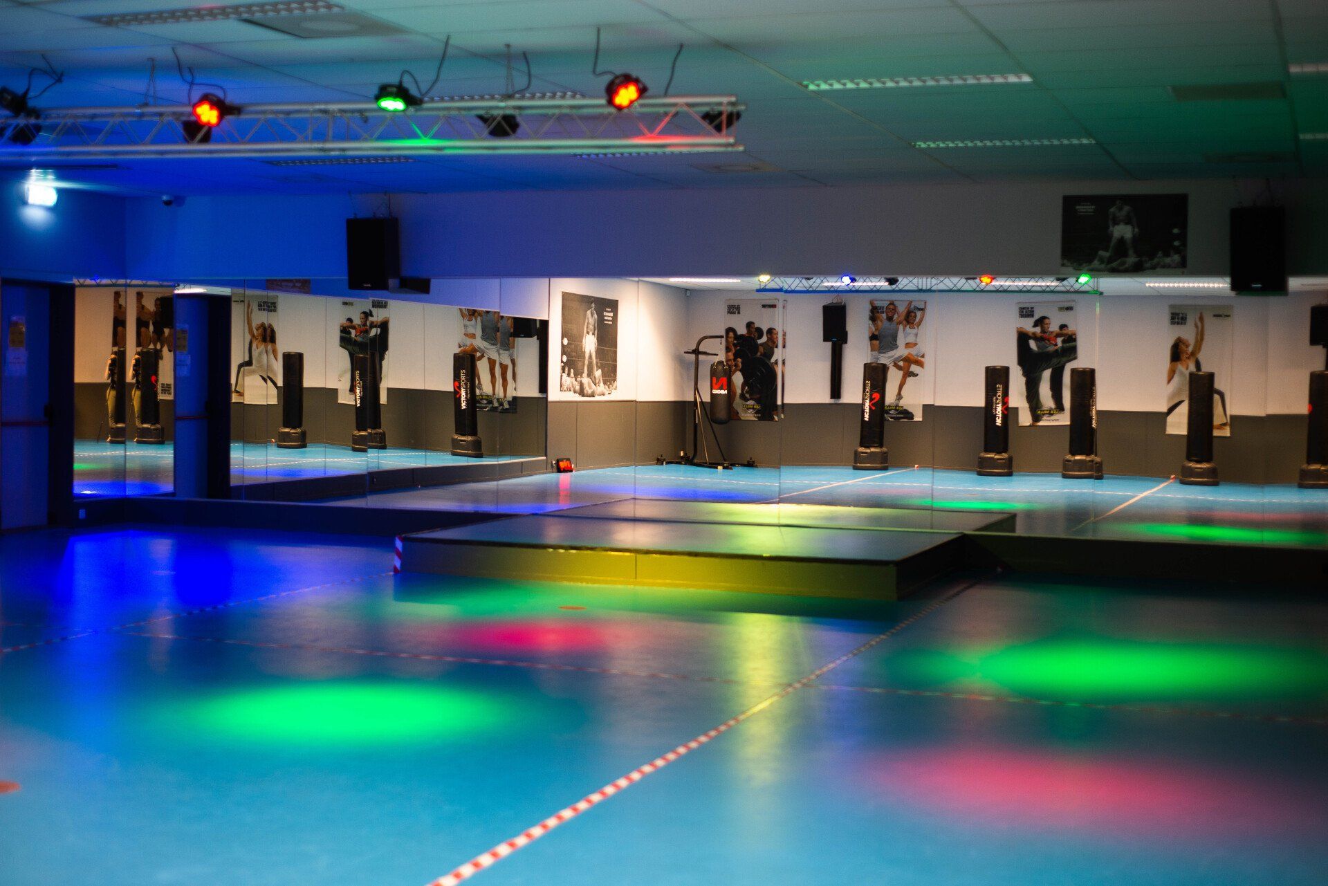 Sportschool met spiegels, bokszakken en een podium verlicht met blauwe, groene en rode lichten.