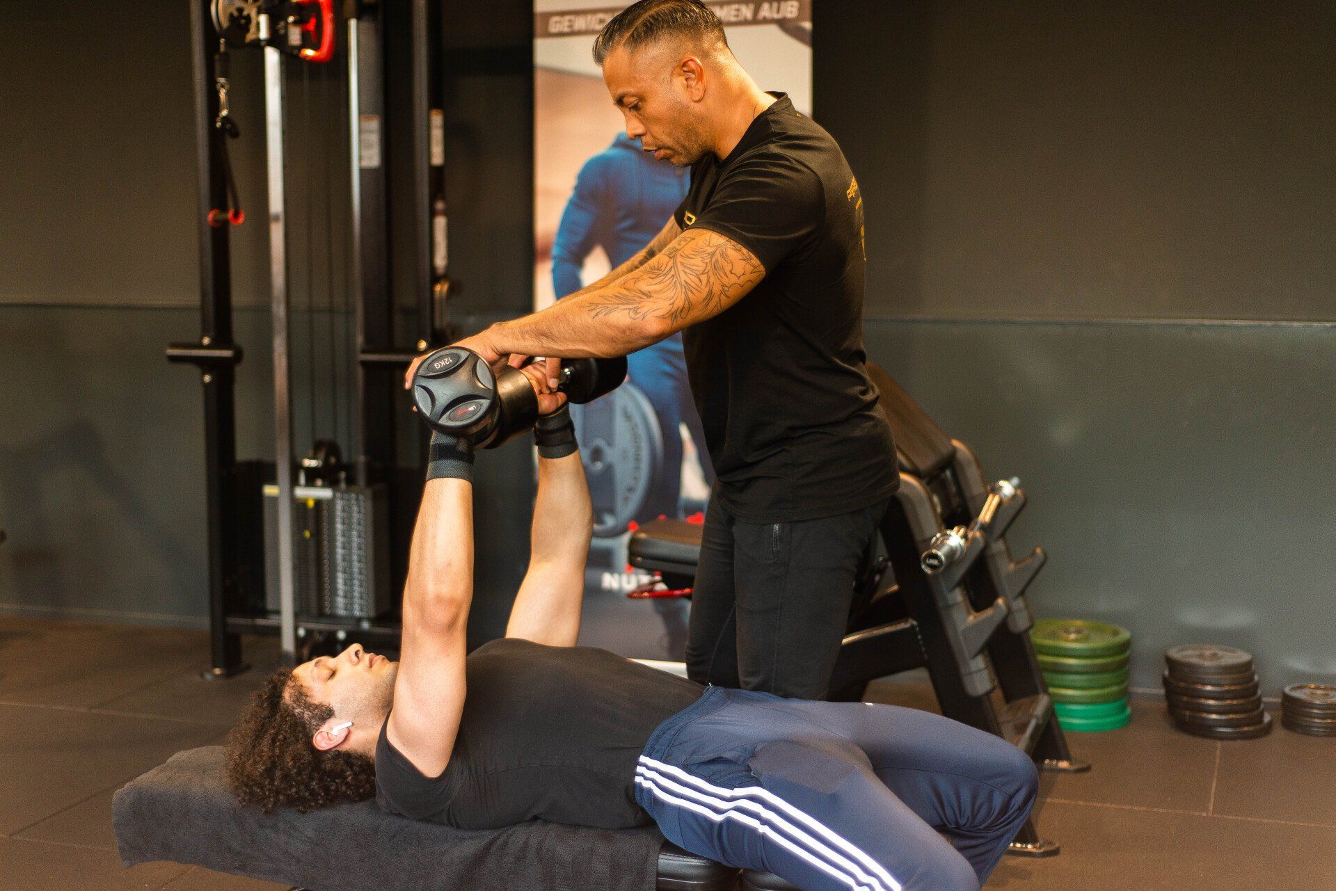 Man wordt in de sportschool door een trainer geholpen bij het doen van een dumbbell chest press.
