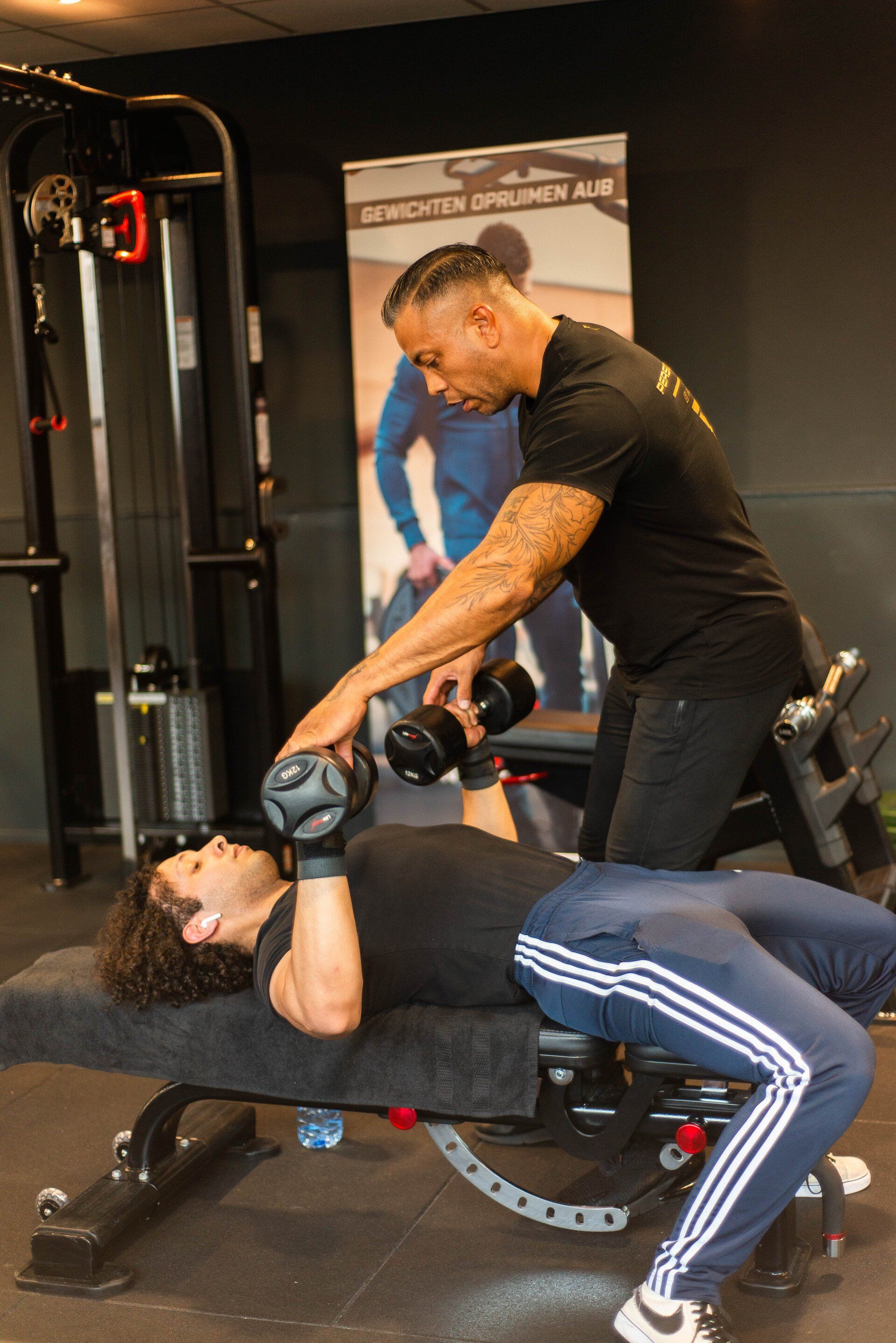 Man helpt een andere man met dumbbell chest press in de sportschool.