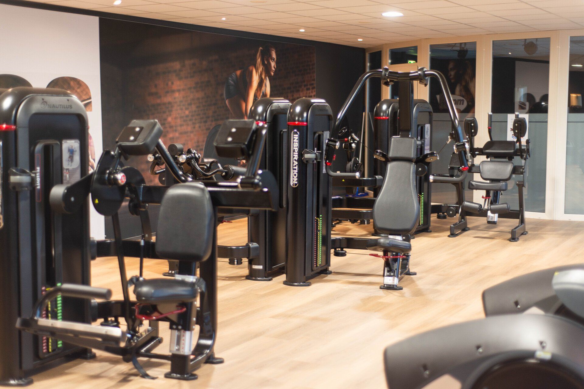 Sportschool met fitnessapparaten, houten vloer, donkere apparaten tegen een achtergrond van een muurschildering met een gespierd persoon.
