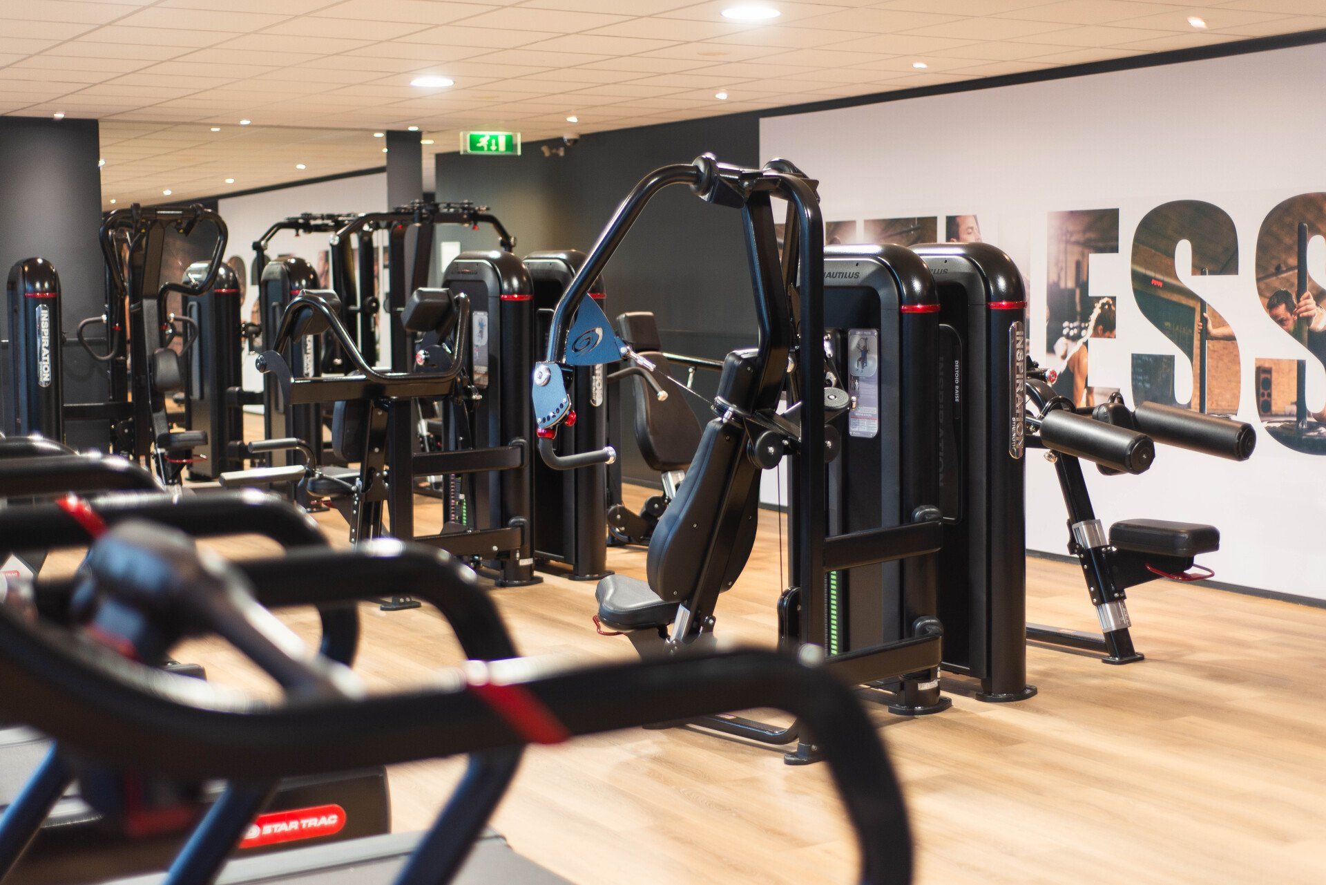 Een sportschool met veel fitnessapparatuur en een muur met de tekst fitness.
