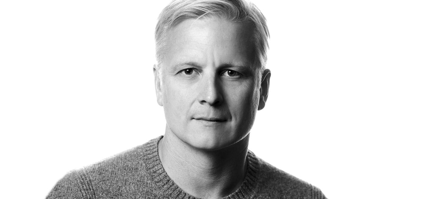 A man in a sweater is looking at the camera in a black and white photo.