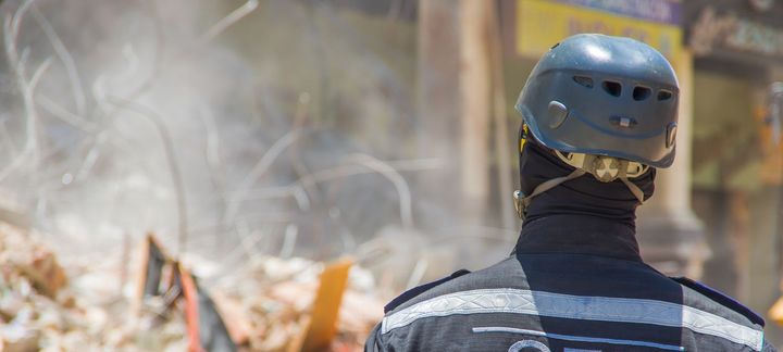 A fireman wearing a helmet is standing in front of a pile of rubble.