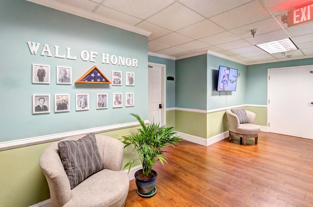A hallway with a chair and a plant in front of a wall of honor.