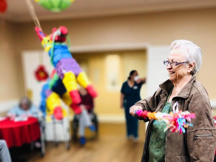 An elderly woman is playing with a pinata in a room.