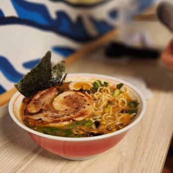 Ramen bowl with pork, seaweed, egg, and noodles, garnished with green onions.