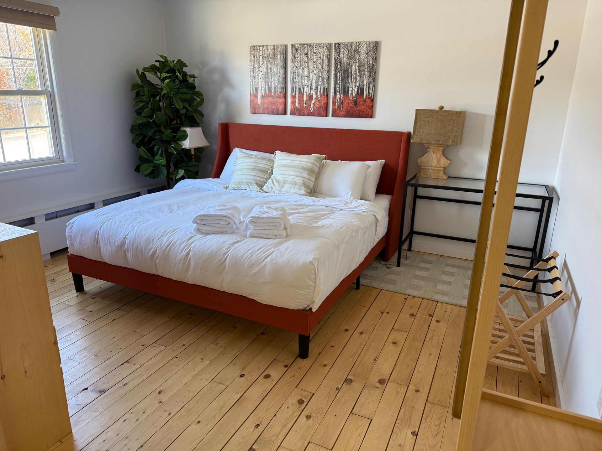 Bedroom with red headboard bed, white bedding, wood floors, and art on the wall.