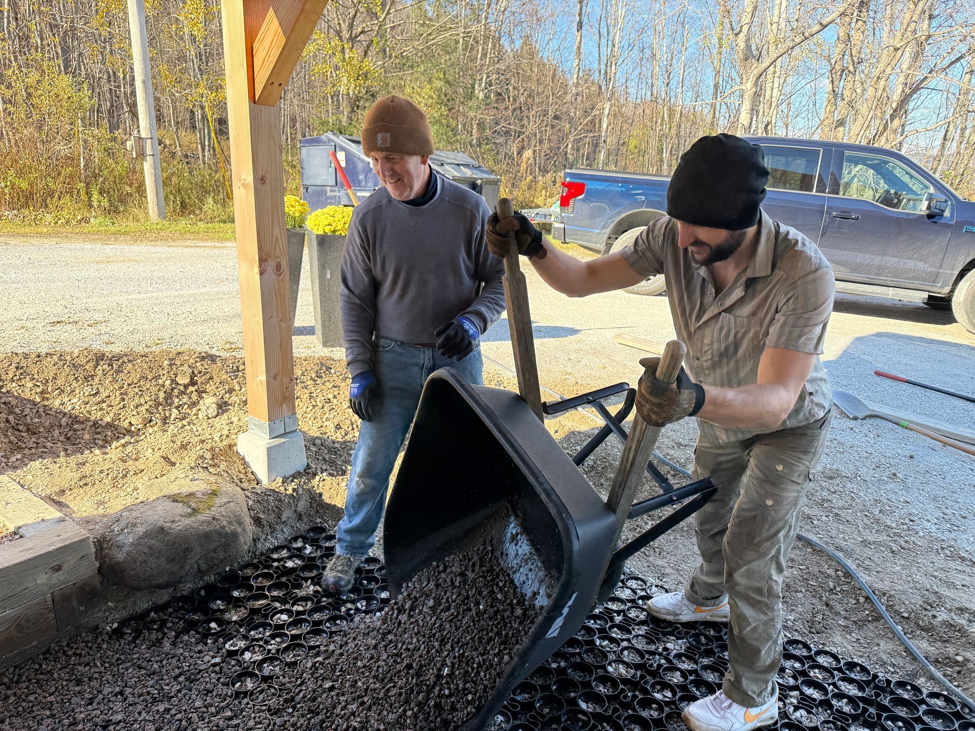 Two people spreading gravel from a wheelbarrow onto a driveway.