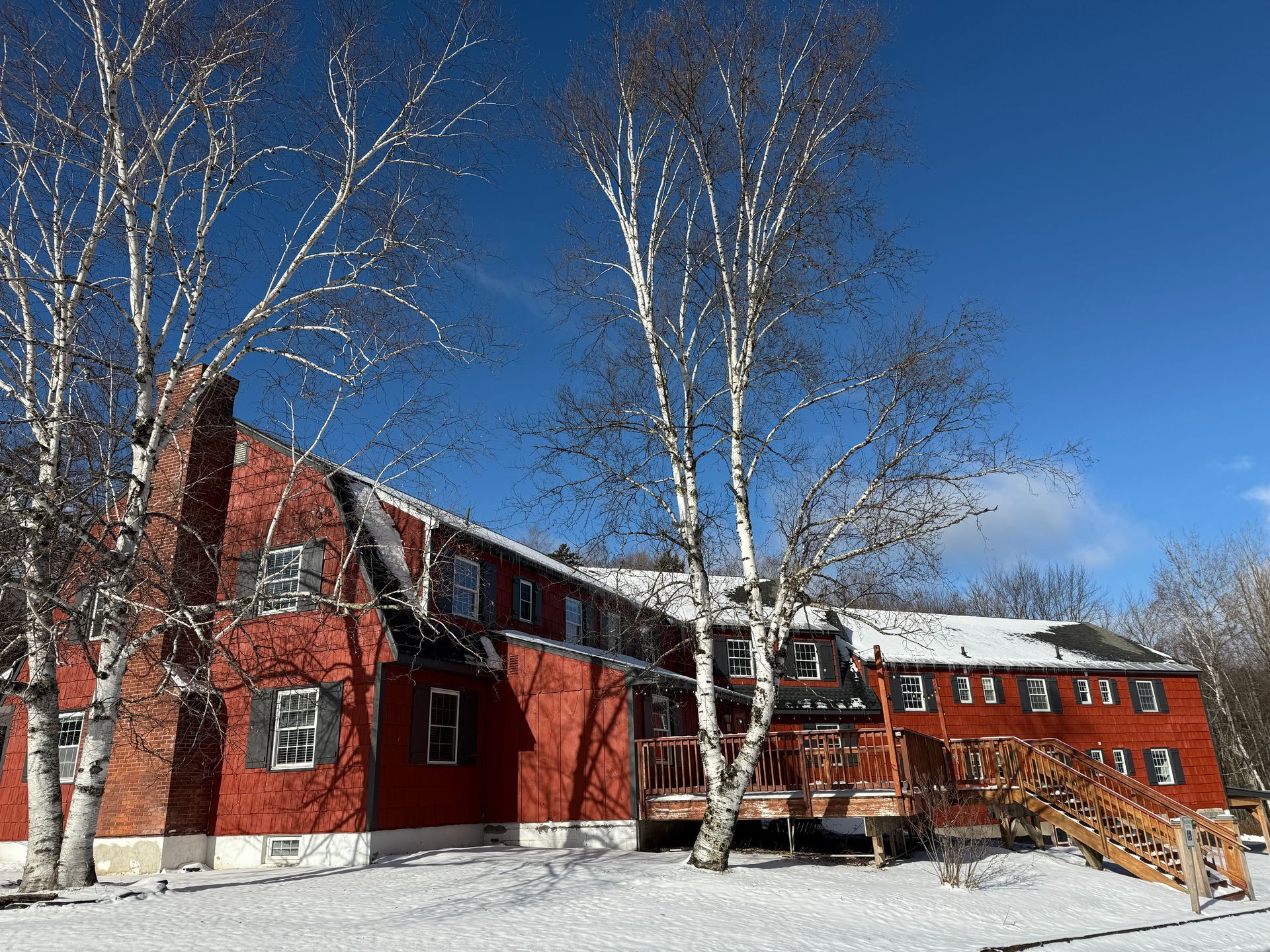 Red building with snowy ground, birch trees, and a clear blue sky.