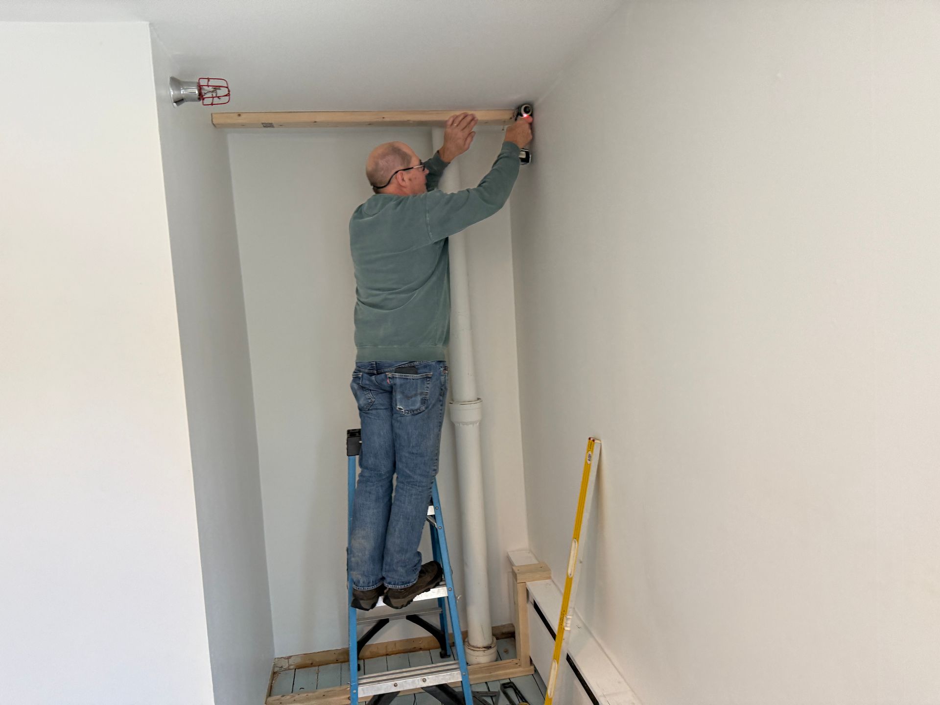 Person on a stepladder installing wood; white walls; level on the wall.