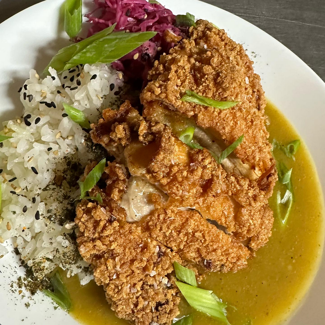 Breaded chicken with rice, cabbage, and a green sauce on a white plate.