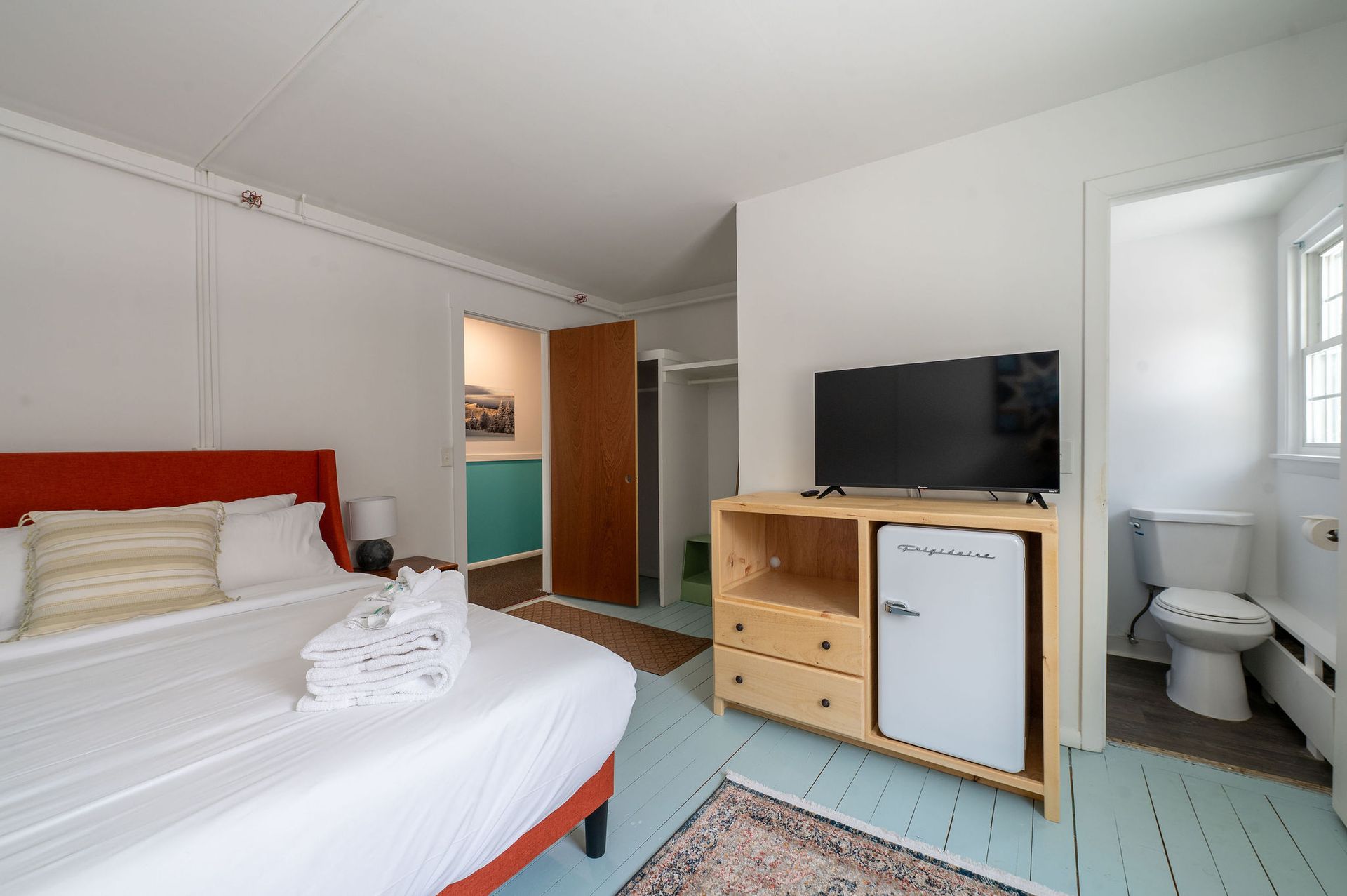 Hotel room with a red headboard, TV, and mini-fridge. Bathroom is visible.