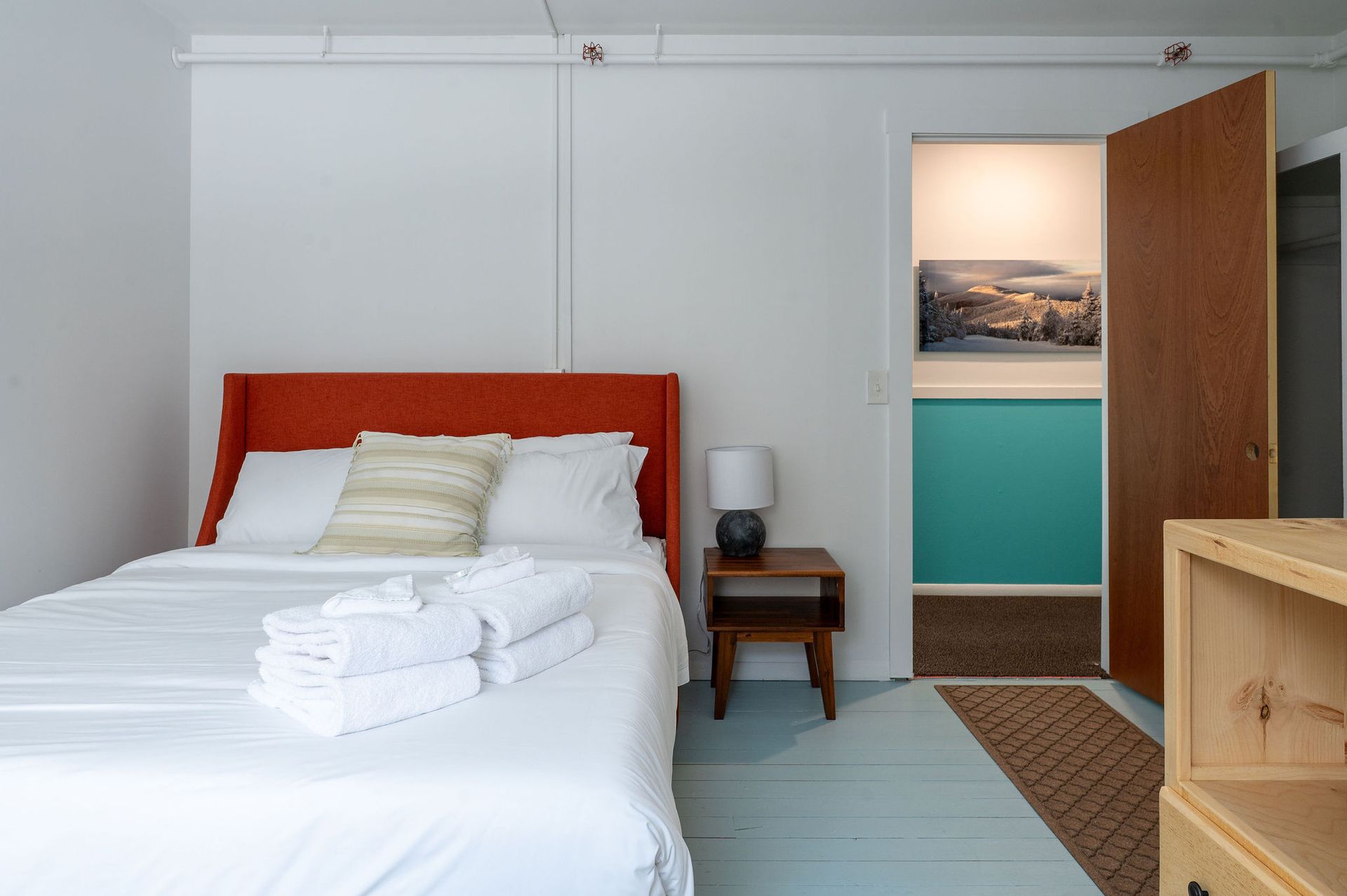 Bedroom with a red headboard, white bedding, and open doorway to another room with turquoise wall.