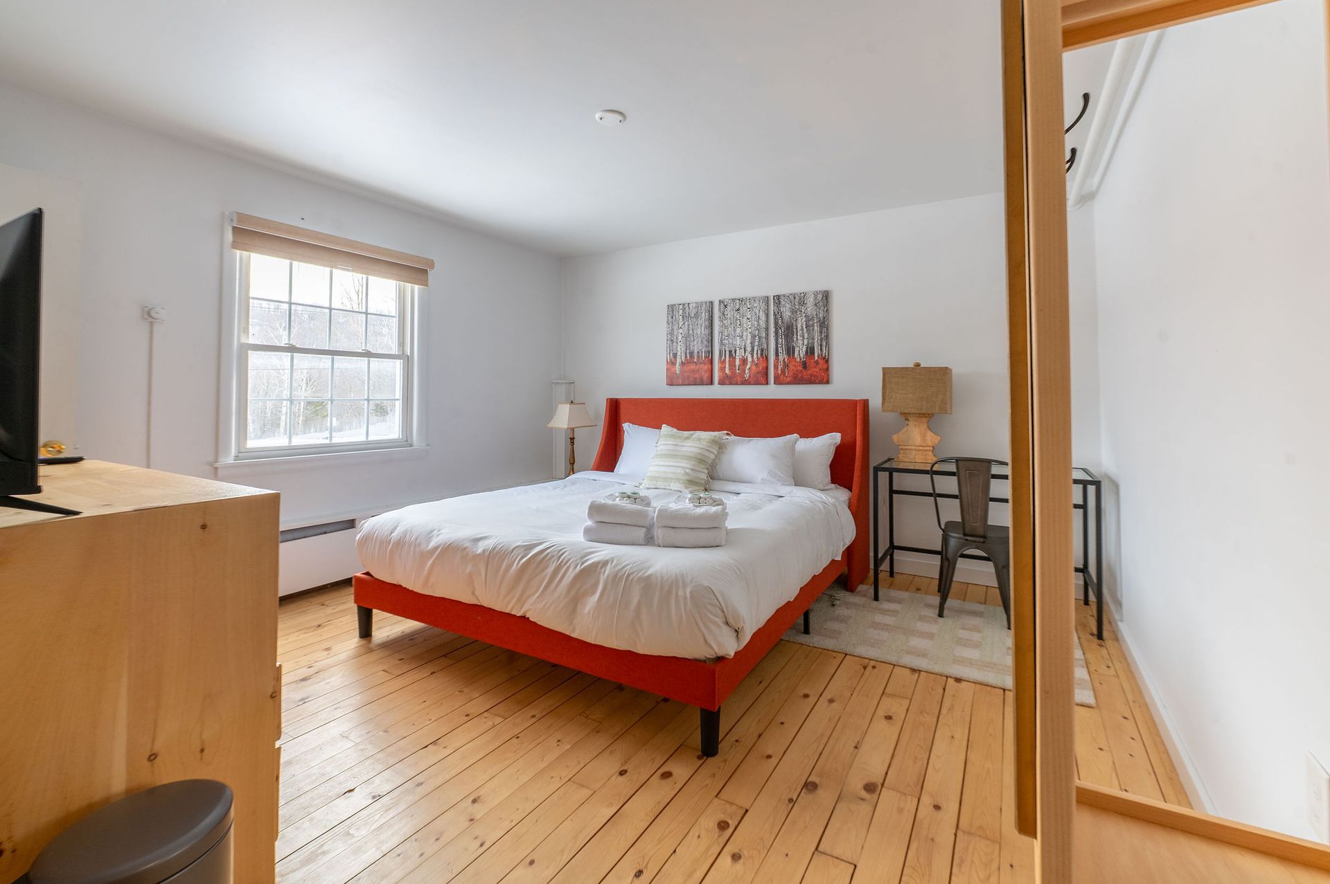 Bedroom with red bed frame, white bedding, wooden floors, and a window.