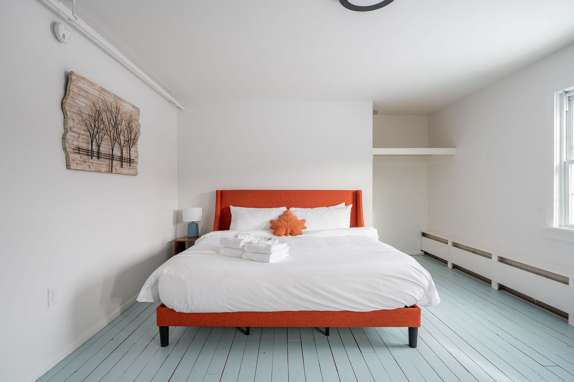Bedroom with orange bed, light blue floor, white walls, and a window.