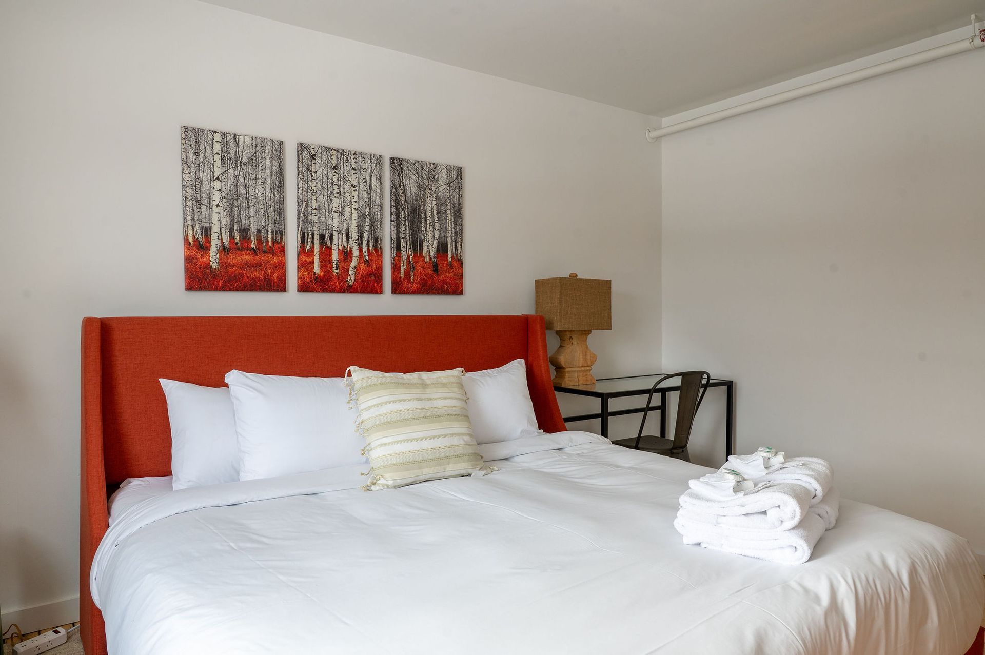 Bedroom with a large orange headboard bed, white bedding, and artwork above.