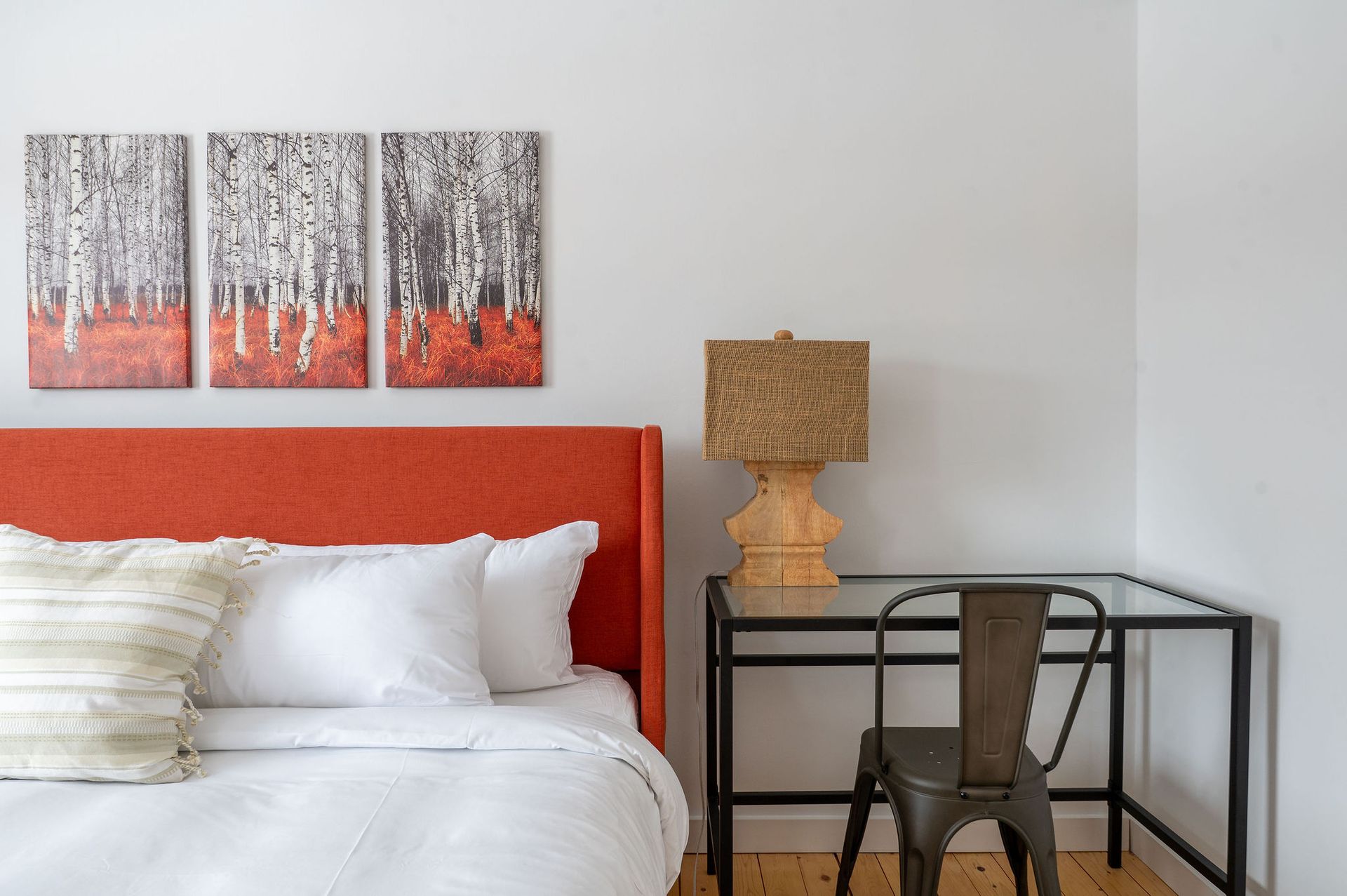 Bedroom with red headboard, white bedding, desk, and tree artwork.