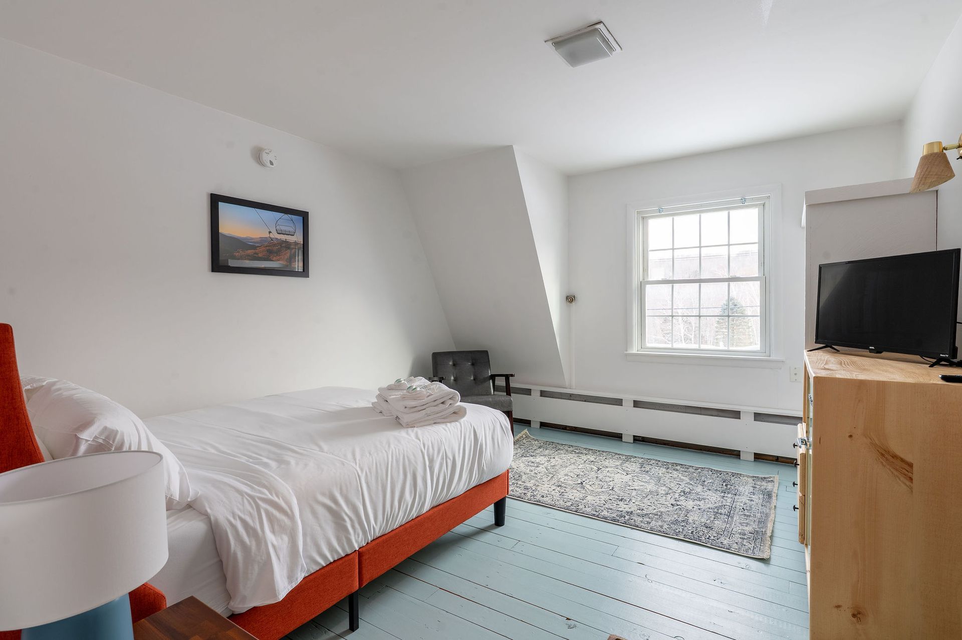 Bedroom with white walls, bed, window, TV, and blue painted floor.
