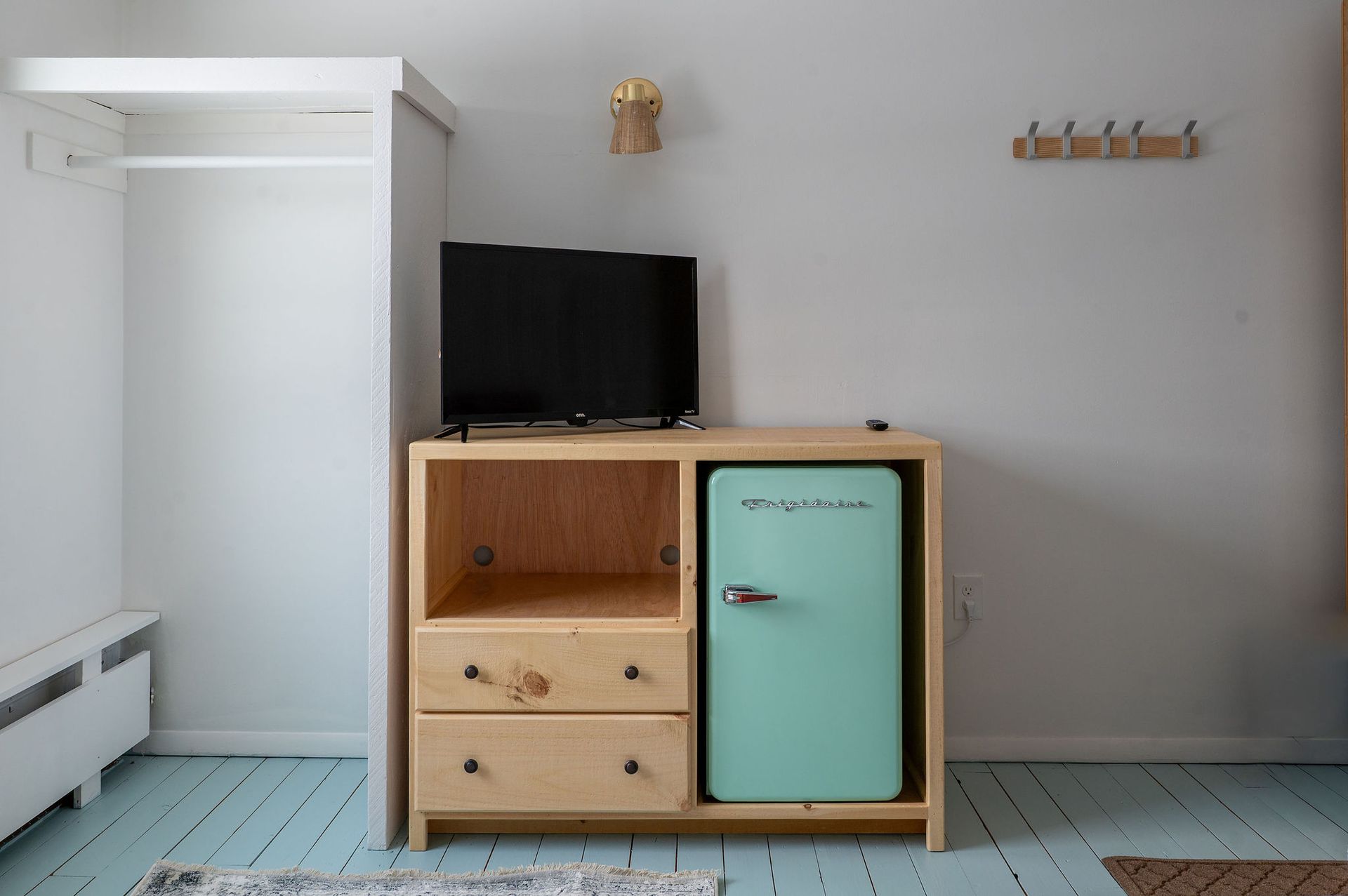 Room with light blue floor. Wooden cabinet holds a small TV, drawers, and a mint-green refrigerator.