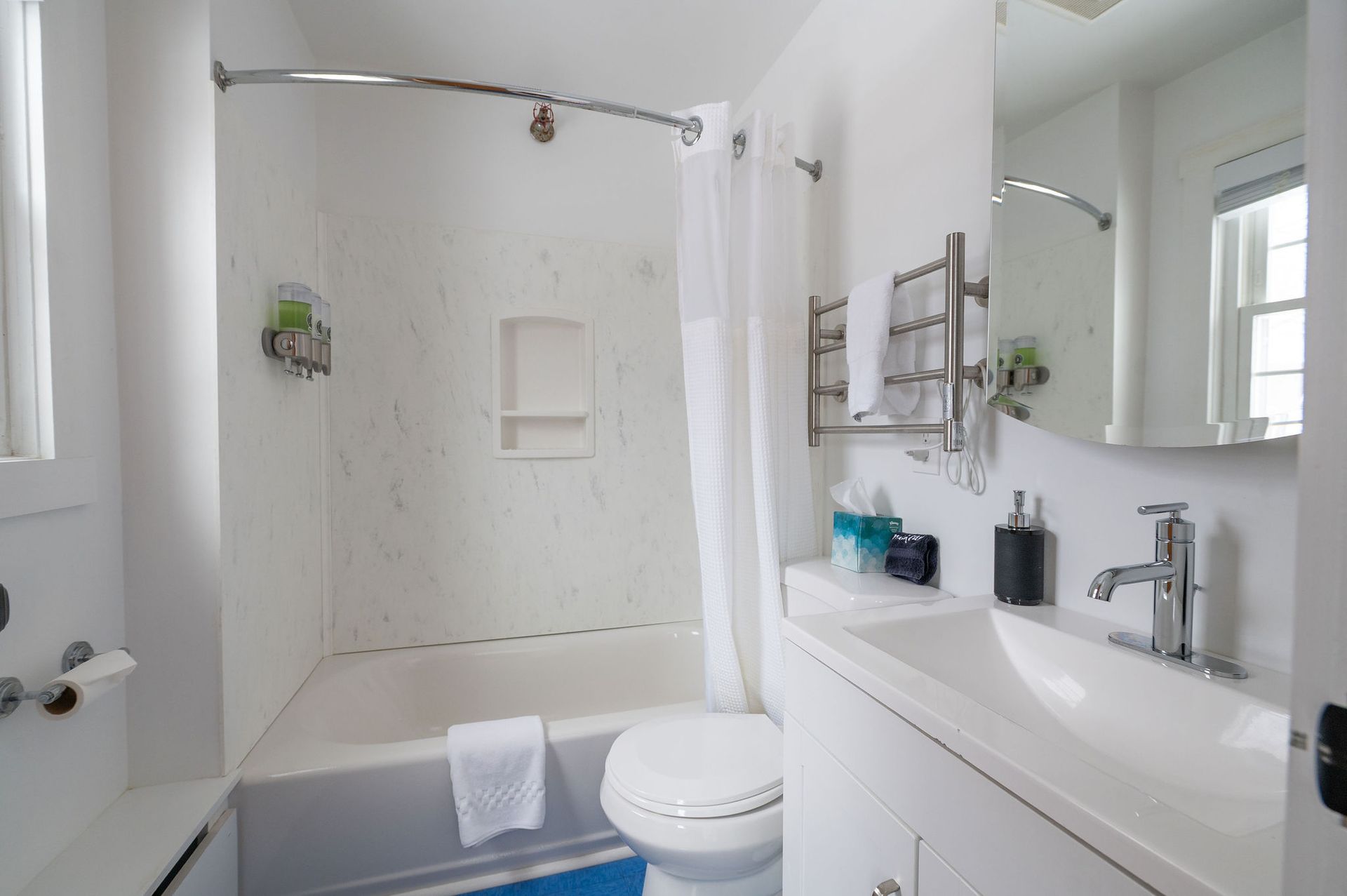White bathroom with a bathtub, toilet, sink, and window.