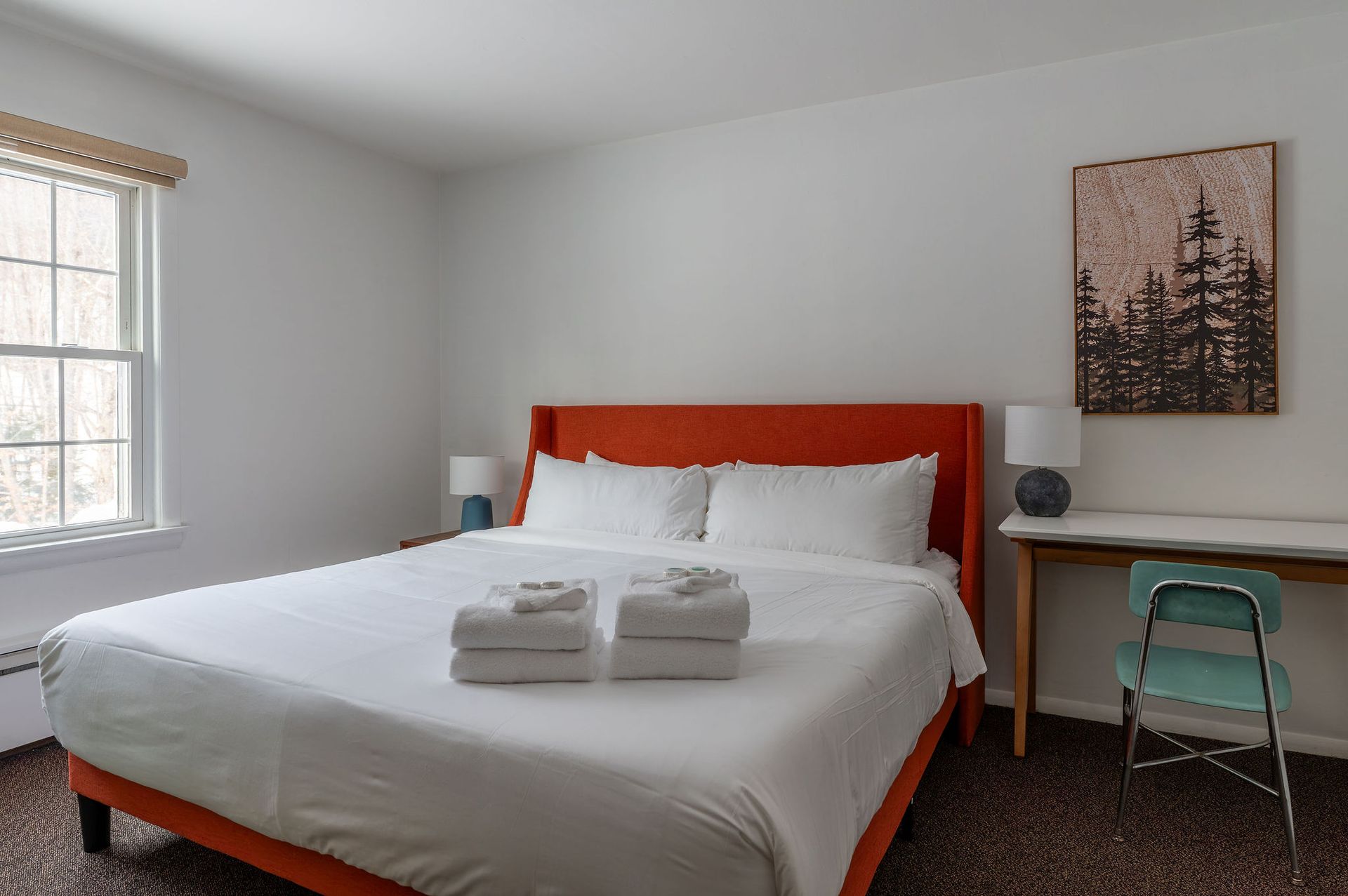Bedroom with a king bed, orange headboard, small desk, chair, window, and wall art.