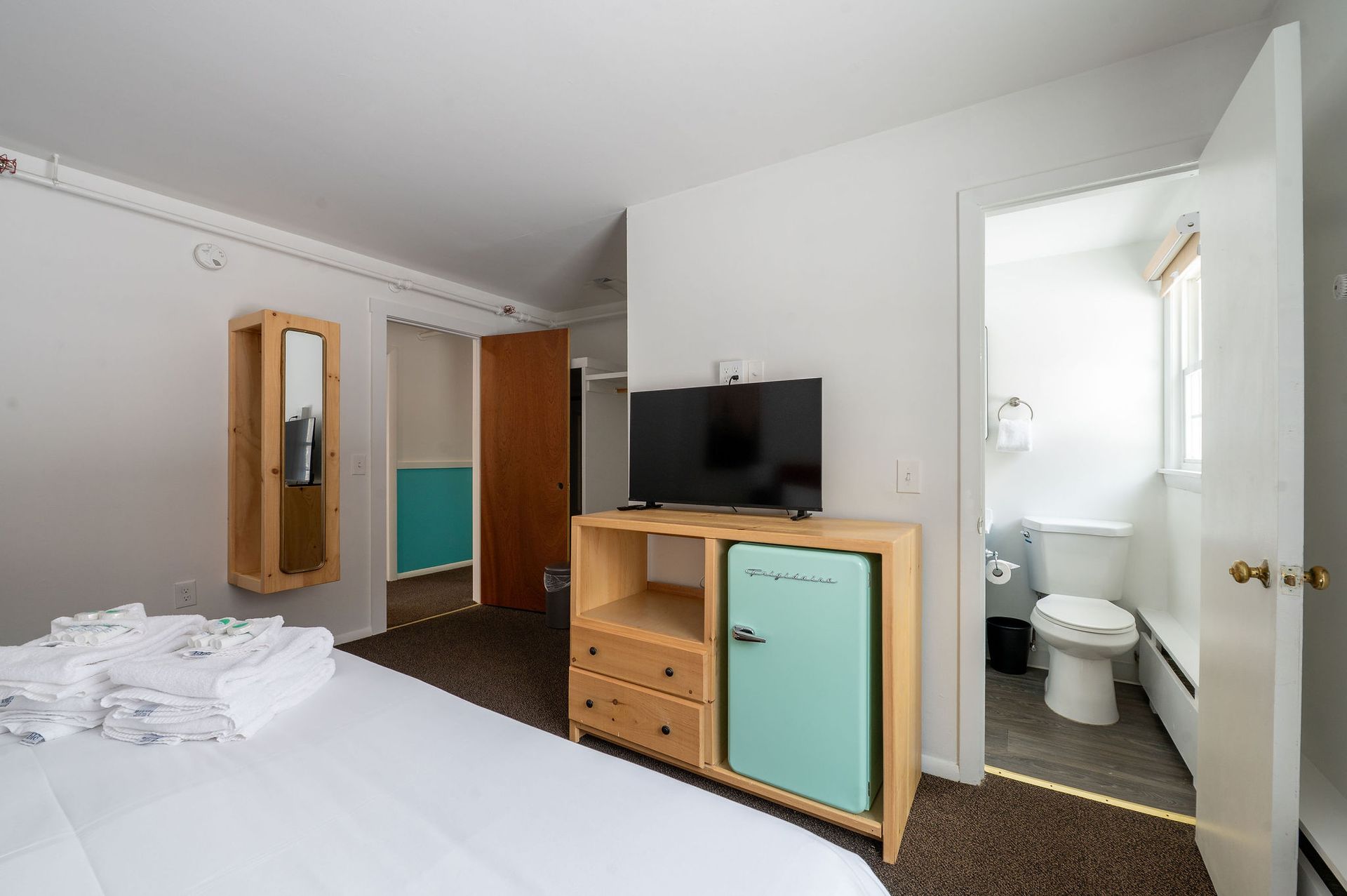 Bedroom with bed, television, mini-fridge, and bathroom.