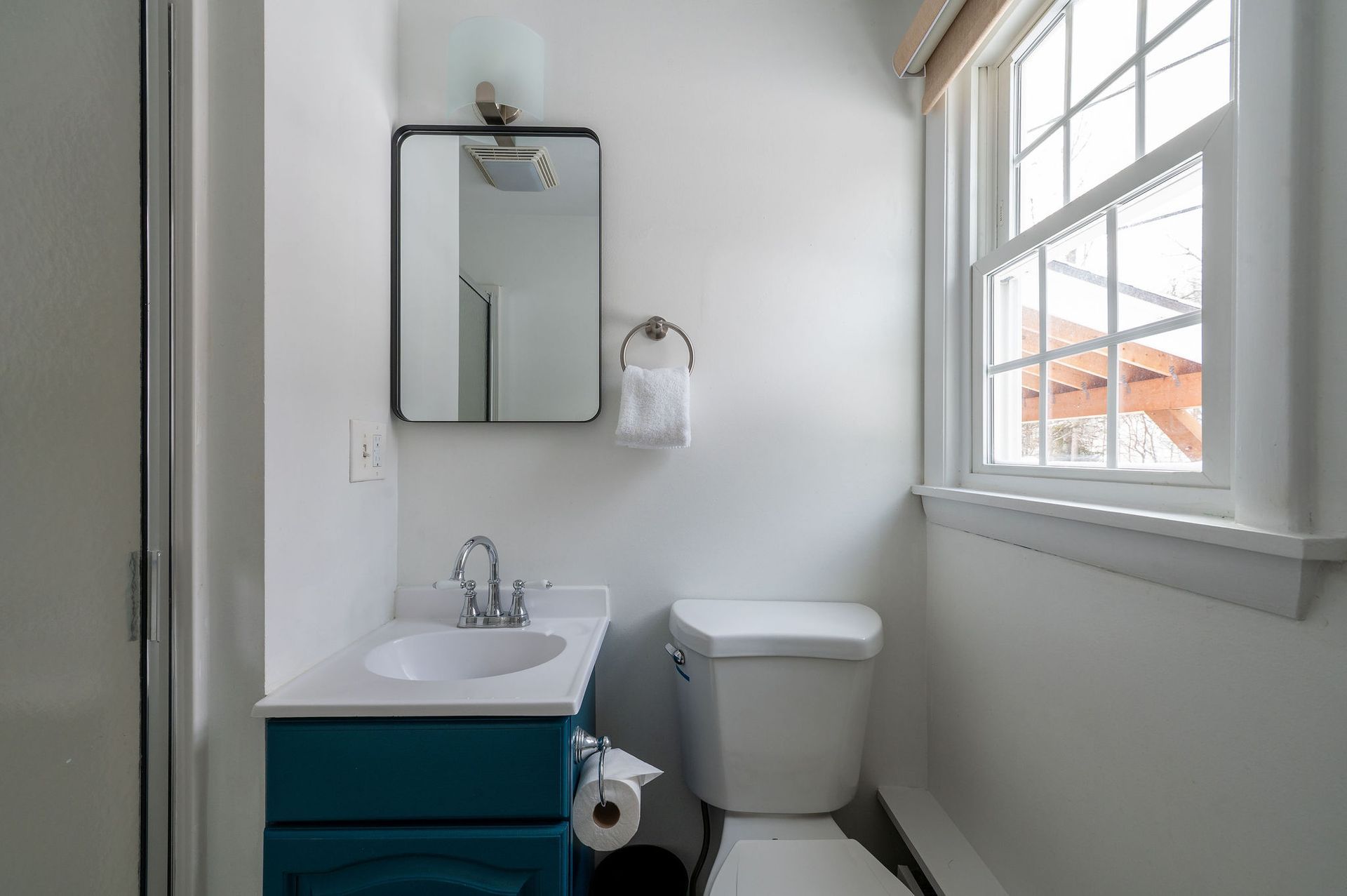 Small bathroom with teal vanity, white toilet, and window.