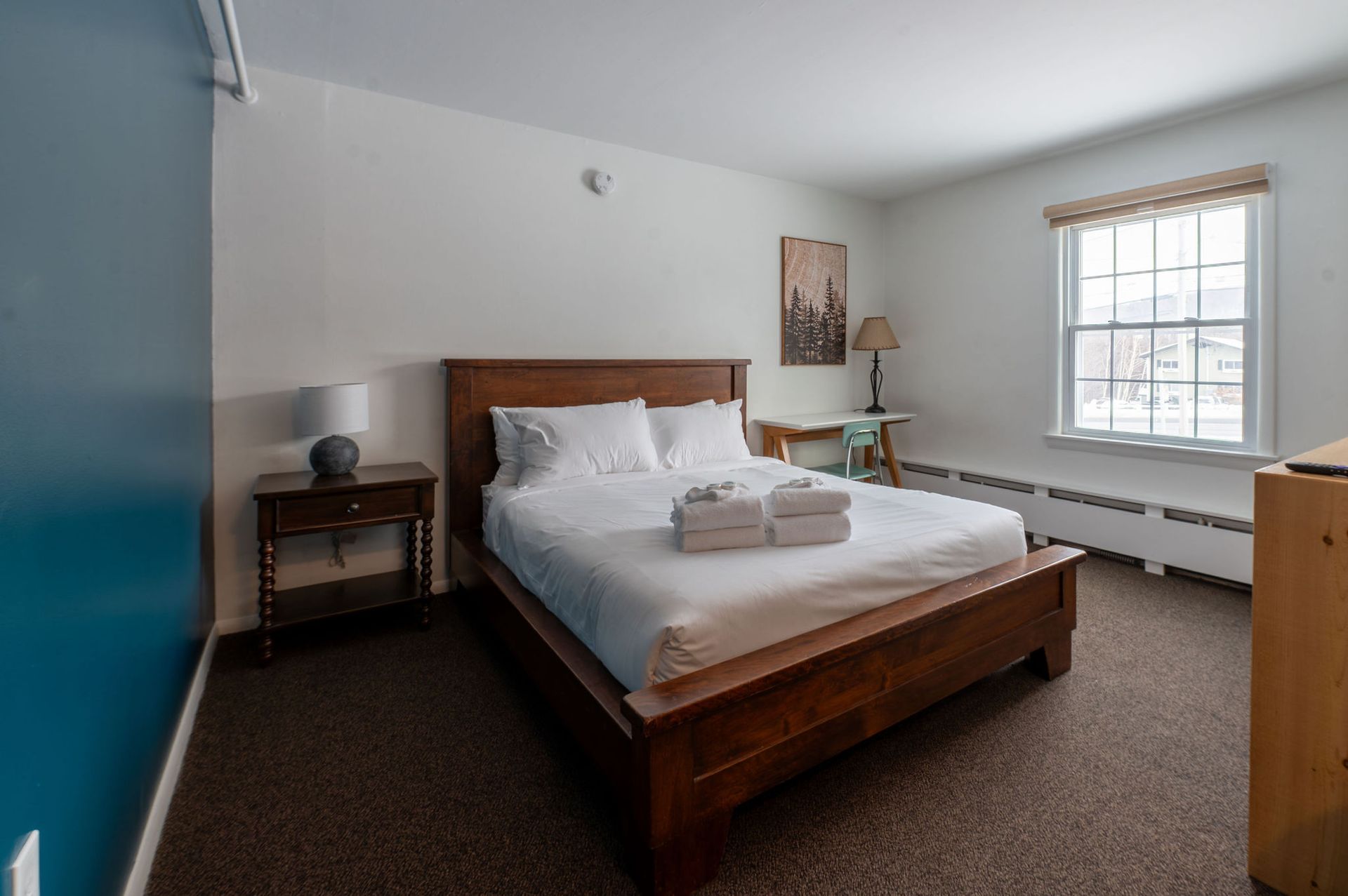 Bedroom with a bed, nightstand, and window. Blue wall on the left, brown carpet, white walls.