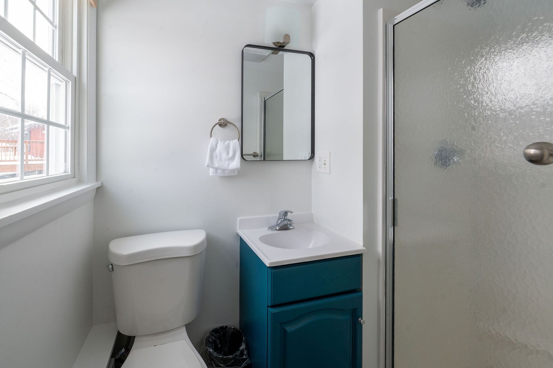 Small, white bathroom with a turquoise vanity, shower, and toilet.