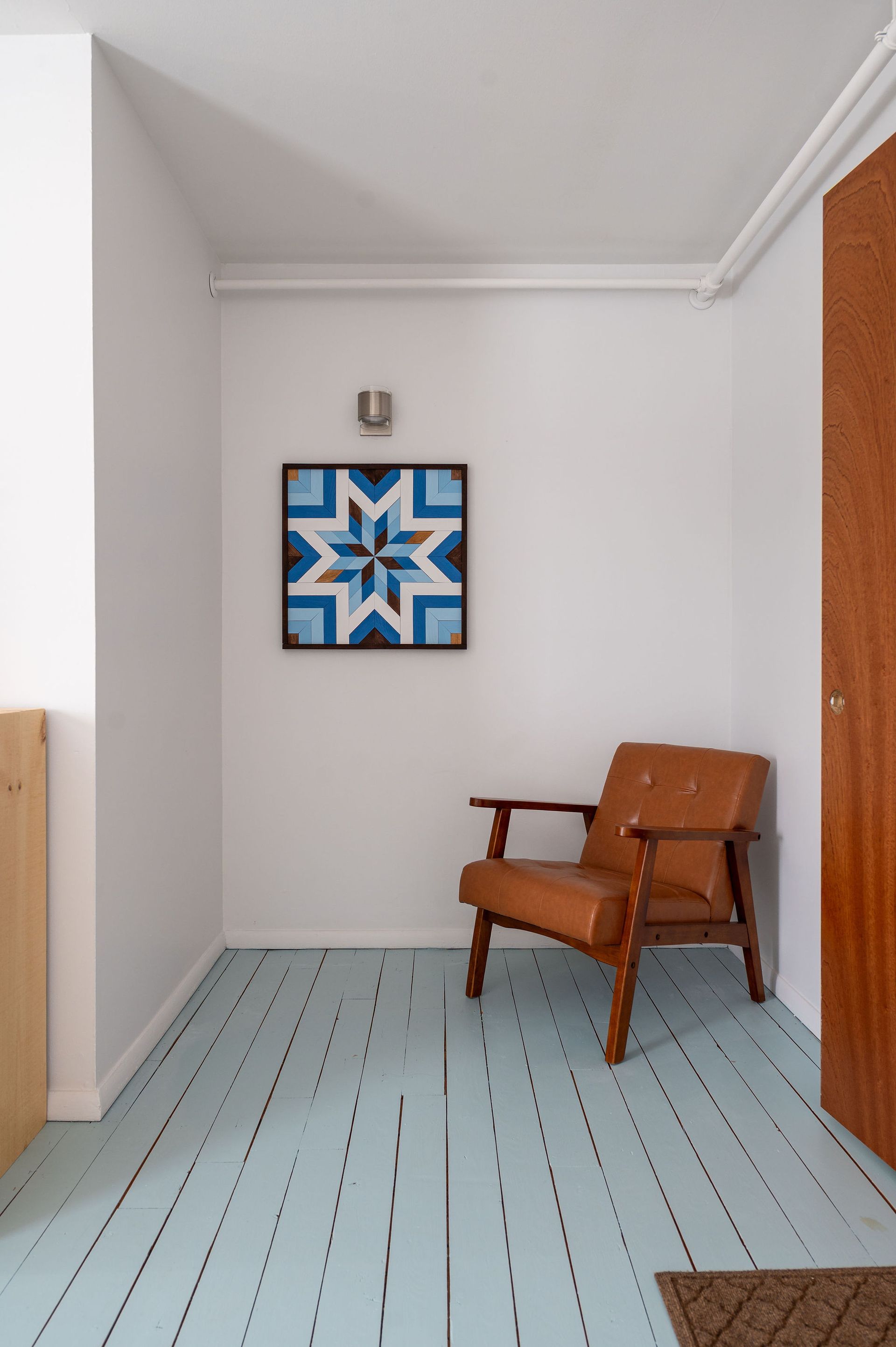 Hallway with a blue-painted floor, a brown armchair, and a star-shaped art piece.