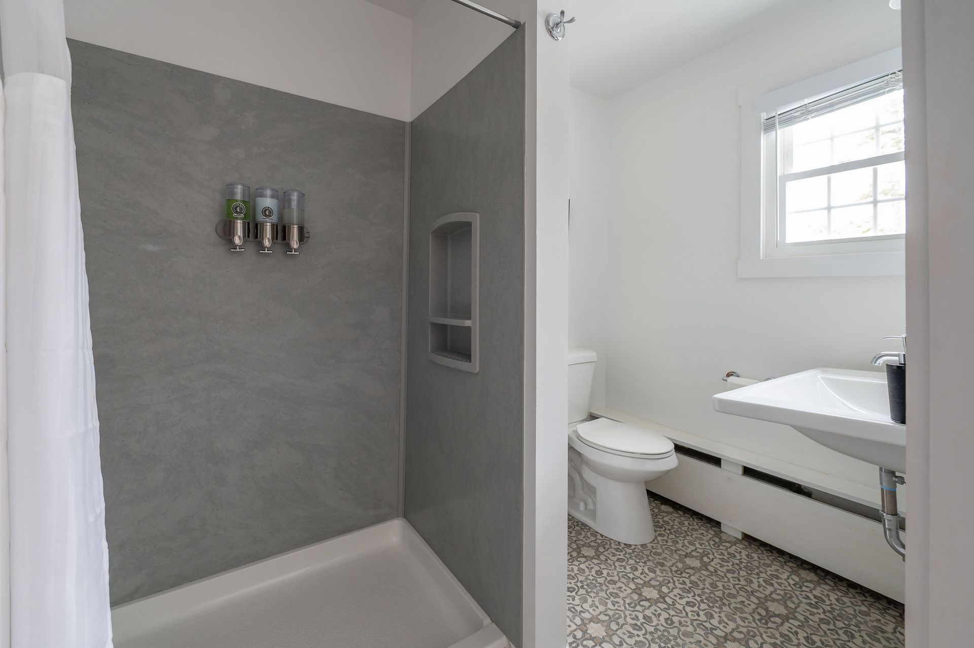 Bathroom with gray shower, white walls, toilet, sink, and patterned floor.