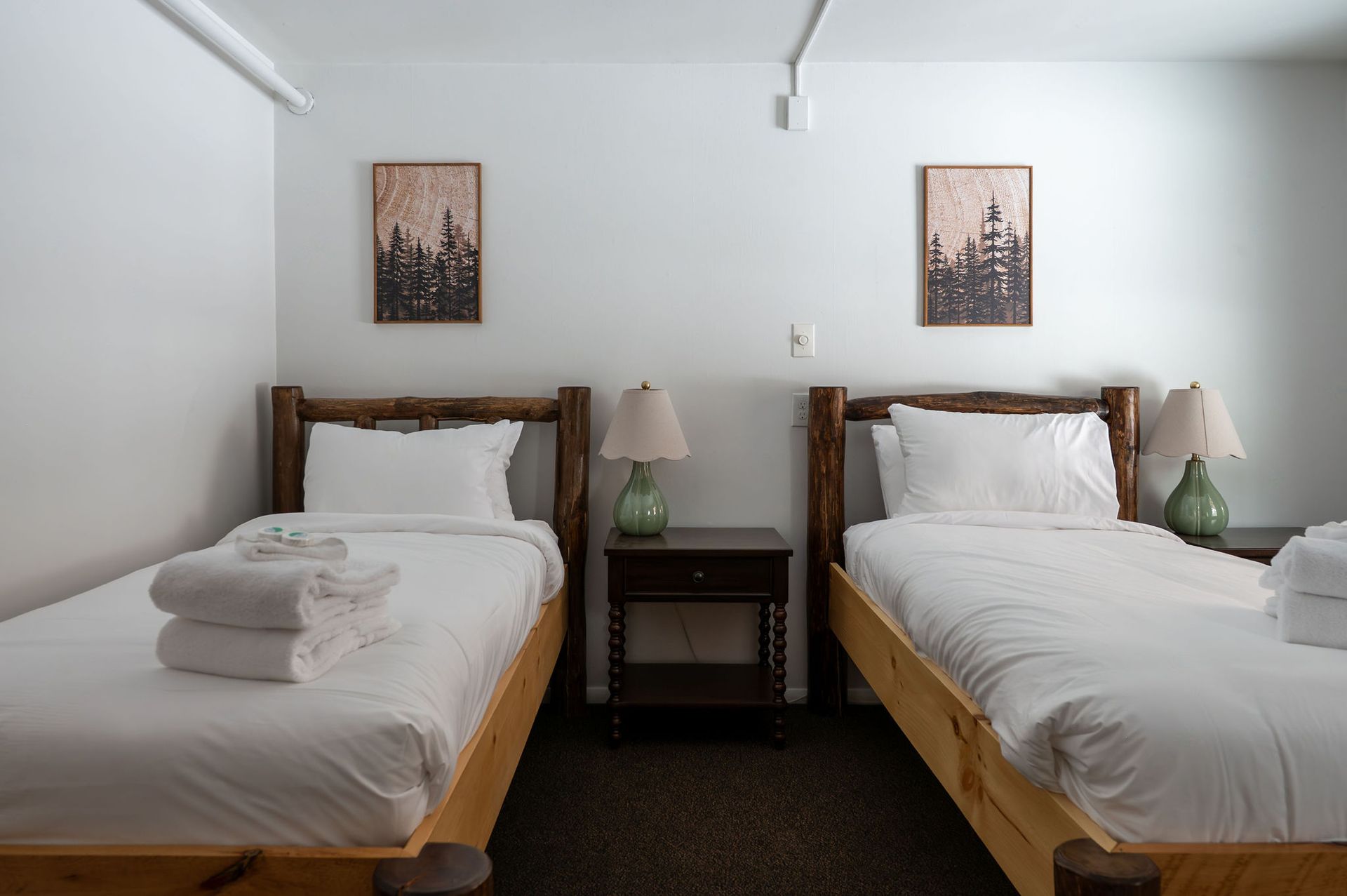 Two beds in a room, each with white linens. Nightstands and lamps are between the beds. Artwork on the wall.
