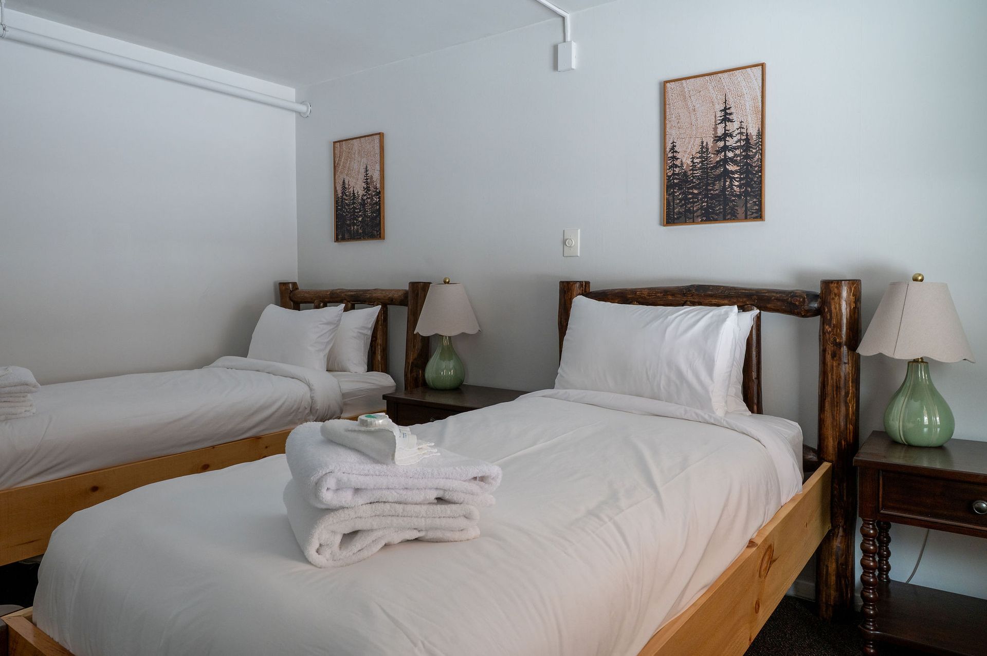 Bedroom with two twin beds, white linens, wooden frames, nightstands, and artwork on the walls.