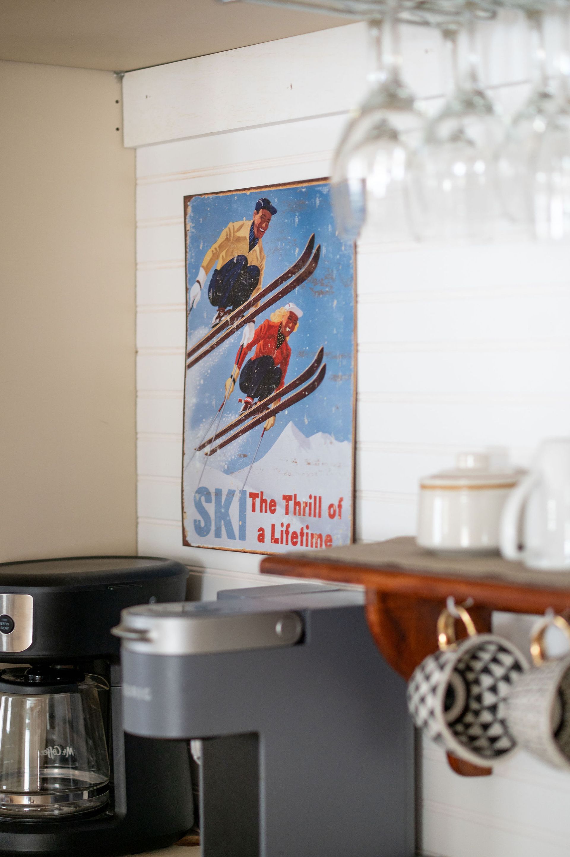 Ski sign with two skiers on a snowy mountain, next to a coffee maker and mugs.