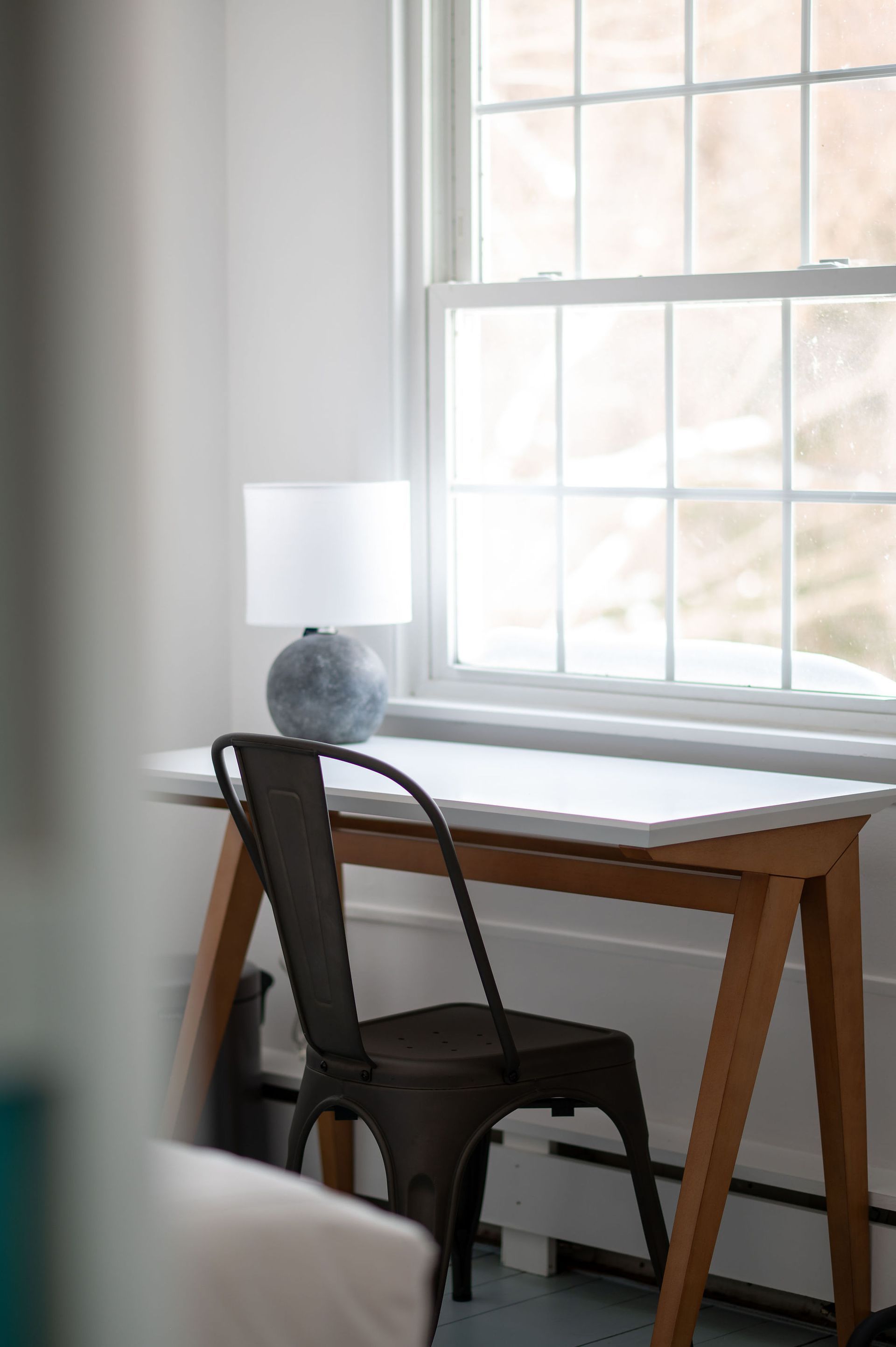 Desk with lamp and chair by a window. Sunlight streams through.