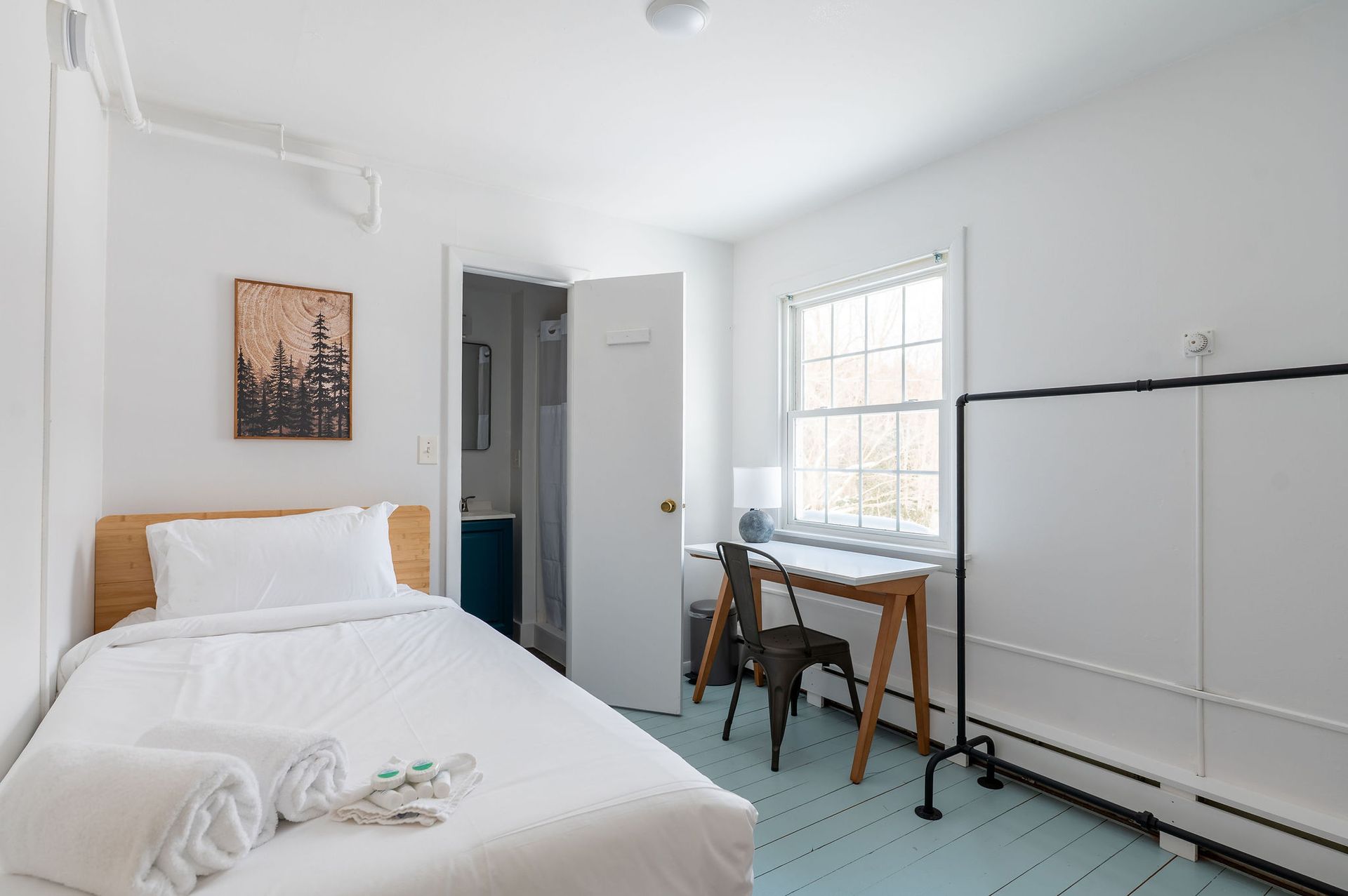 A small, white bedroom with a bed, desk, and closet. A bathroom door is slightly ajar.