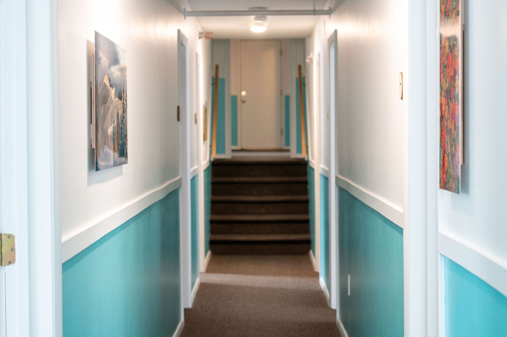 Long hallway with turquoise walls, white trim, and a staircase leading up to a door.