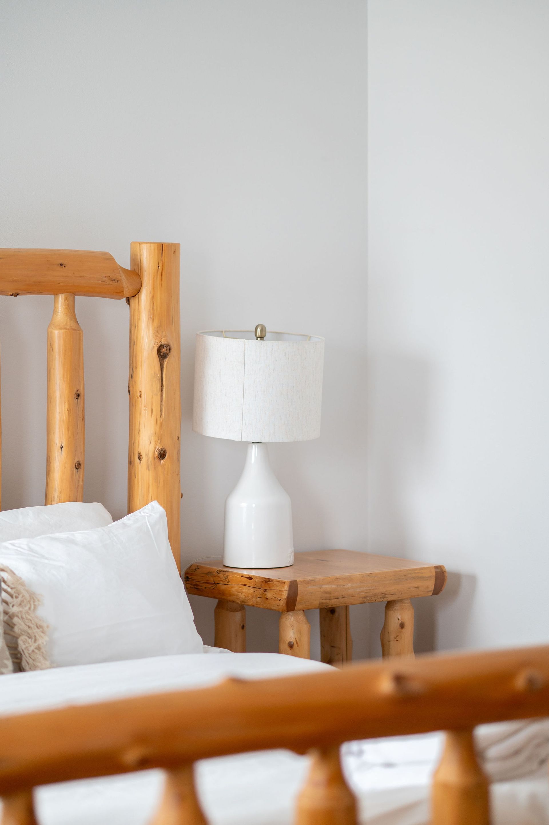 Wooden bed frame and nightstand with a lamp in a light-colored bedroom.