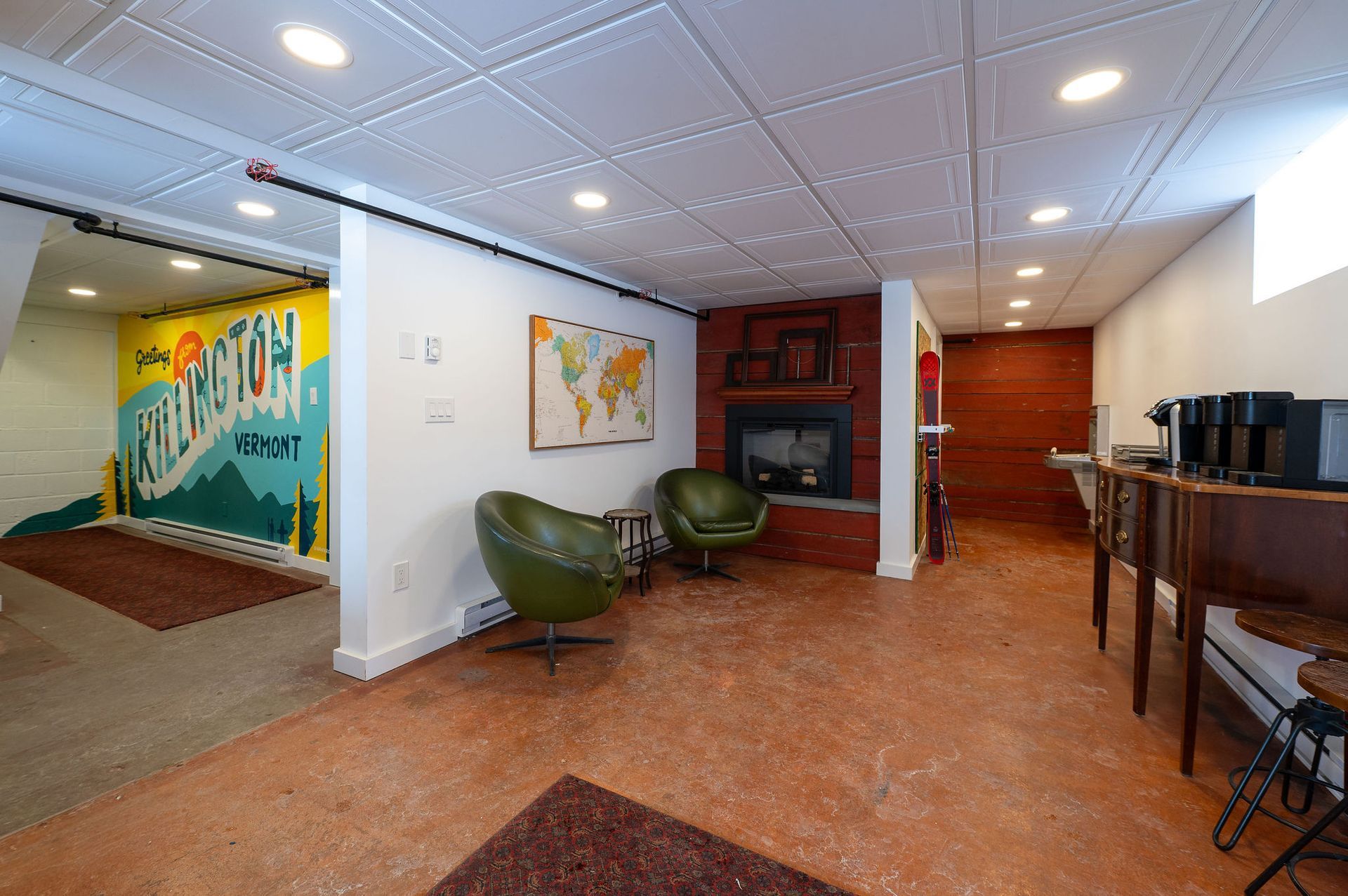 Basement with colorful mural, fireplace, chairs, and coffee station.