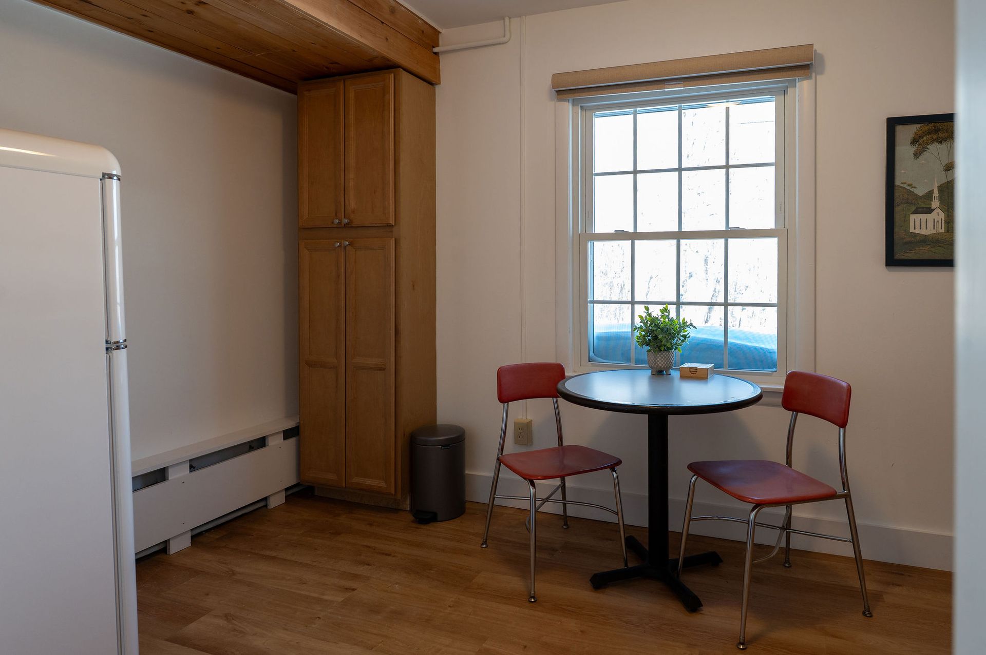 Kitchen with a table, two chairs, a window, tall cabinets, and a refrigerator.