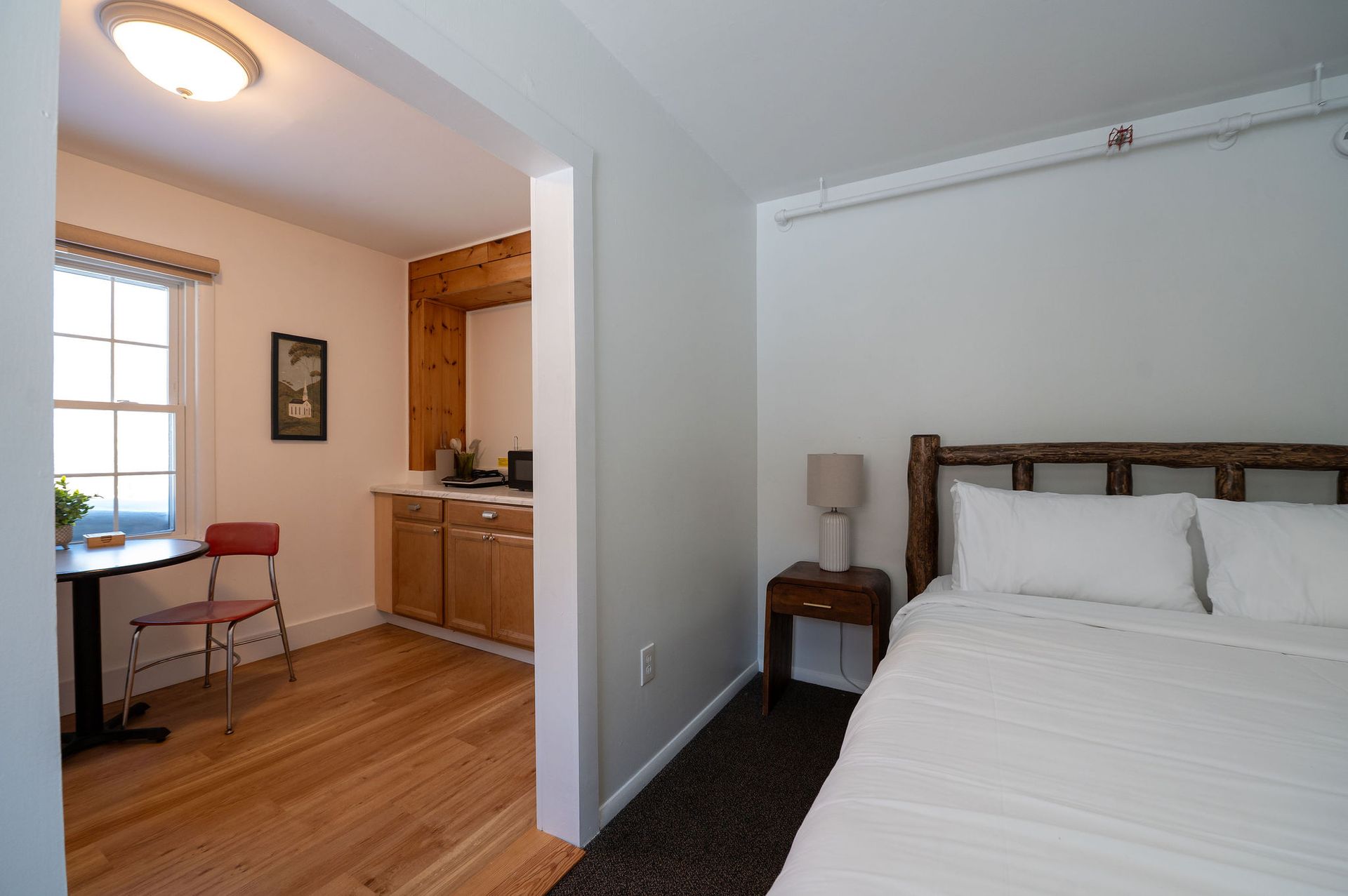 Bedroom with bed, nightstand, and small kitchen area visible through an opening.
