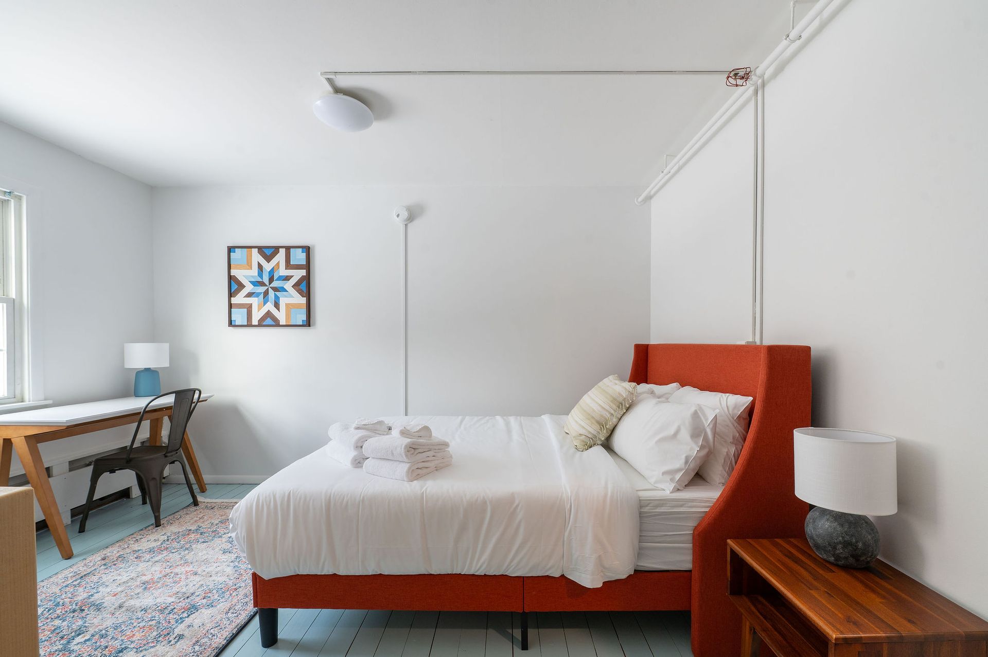 Bedroom with orange headboard, desk, rug, blue and white decor.