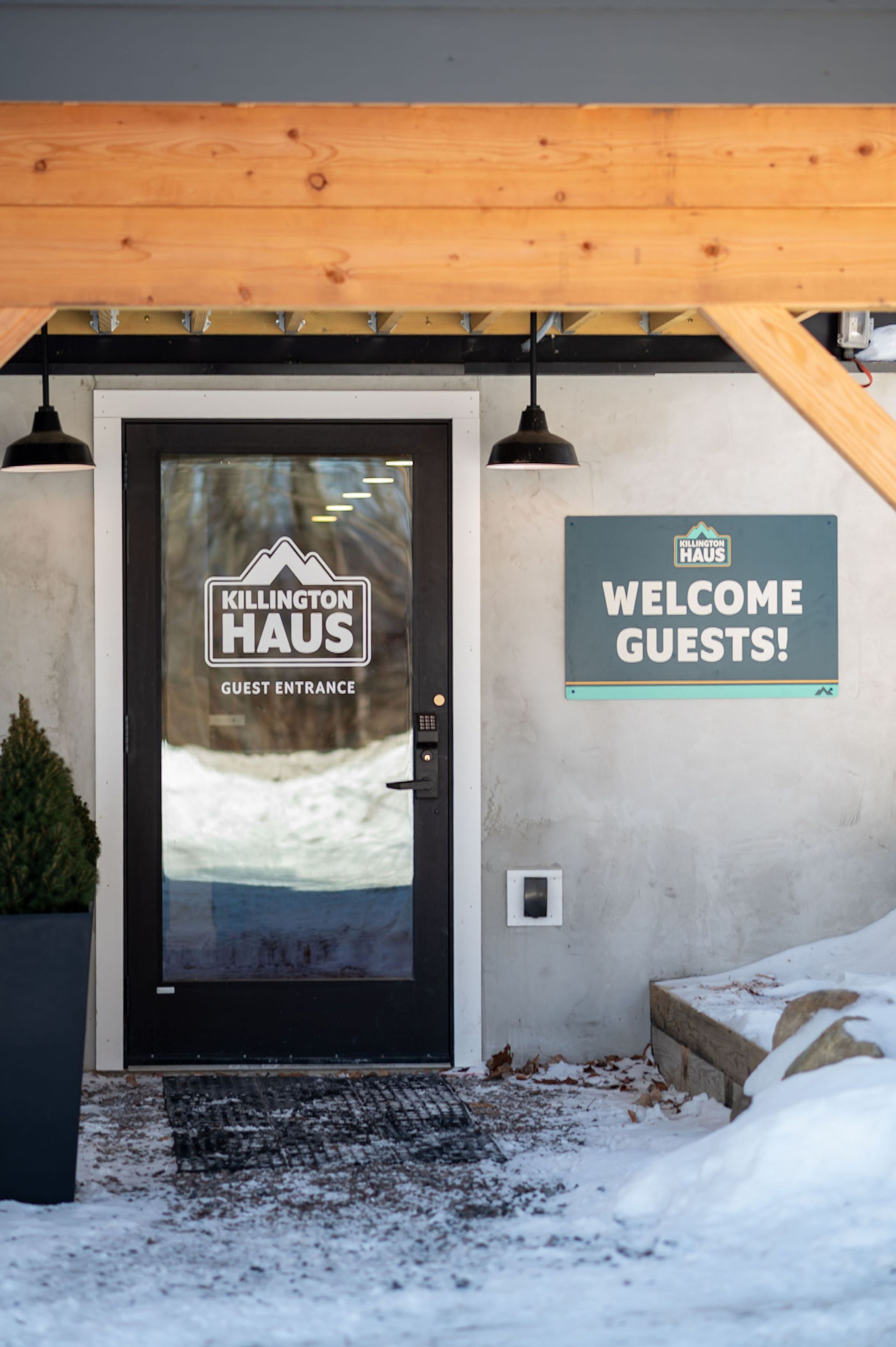 Entrance to Killington Haus with glass door, welcome sign, and snow.