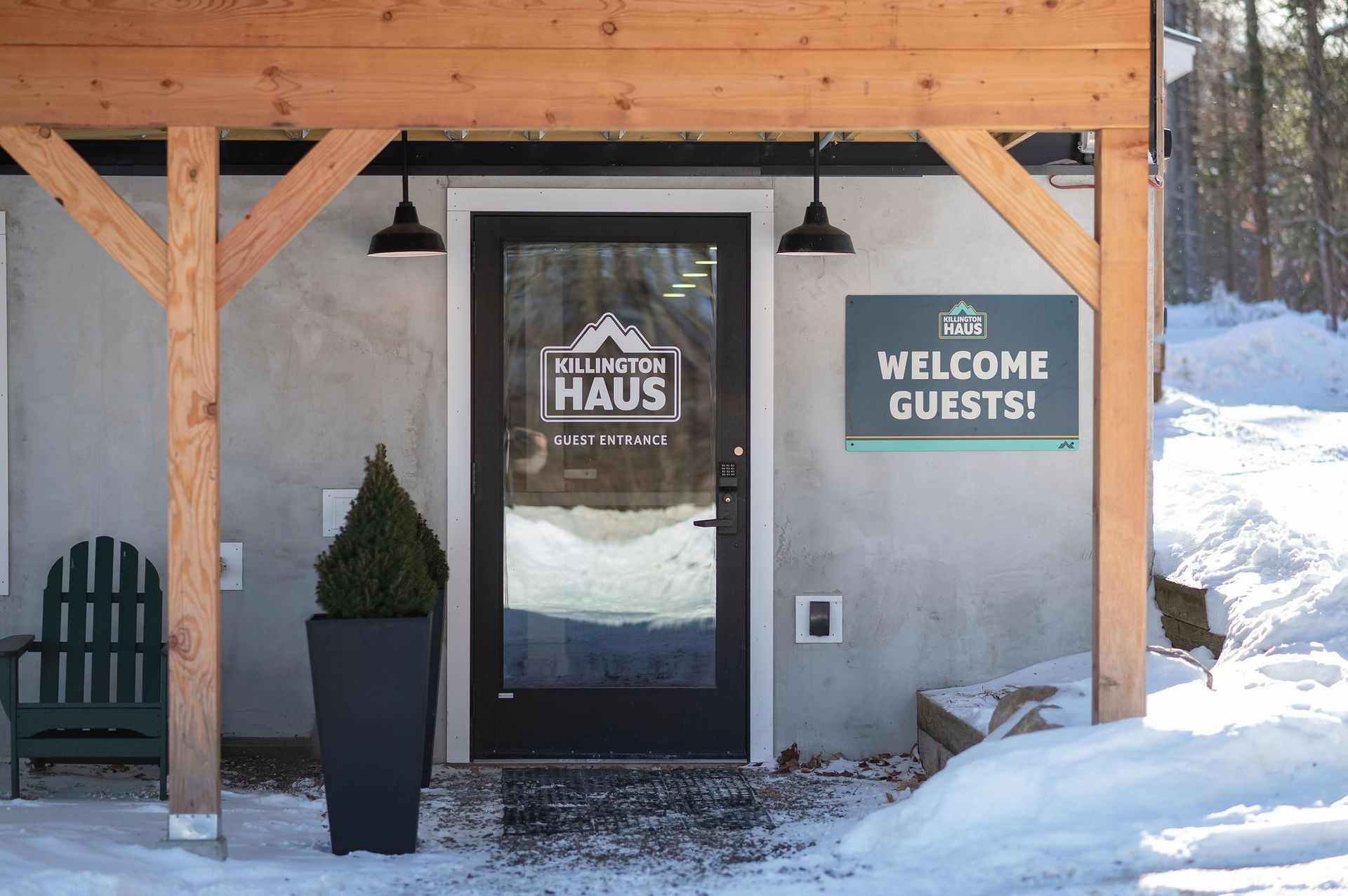 Exterior of Killington Haus entrance, with a clear glass door, welcome sign, and snow-covered ground.