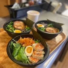 Three bowls of ramen, each with toppings and seaweed, on a wooden tray.