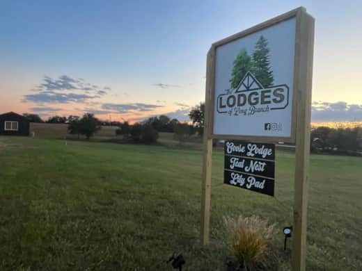 Sign for Lodges of Long Branch in a field with an evening sky; lists three lodge names.