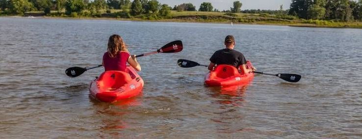 Two people kayaking on a lake. They face away from the camera, paddling through the water.
