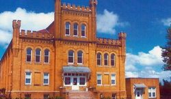 Brick castle-like building with multiple windows and towers against a blue sky with clouds.
